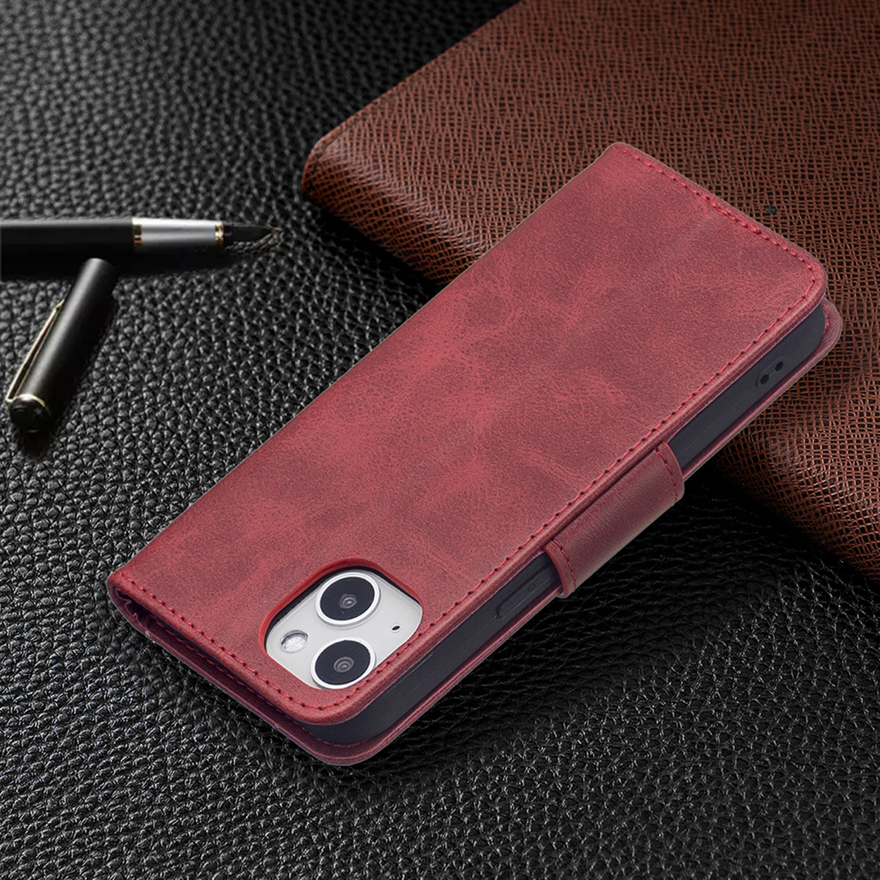 Rode leren telefoonhoes met magnetische flap, op een getextureerd oppervlak, pen en bruine portemonnee zichtbaar.