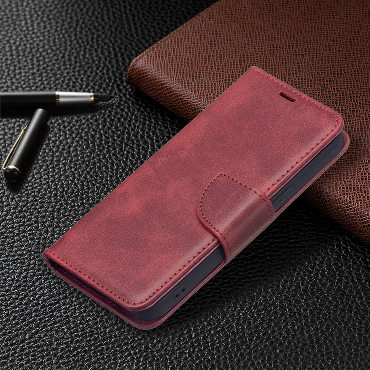 Rode leren telefoonhoes gesloten, met een magnetische sluiting. Een andere bruine leren hoes op de achtergrond.
