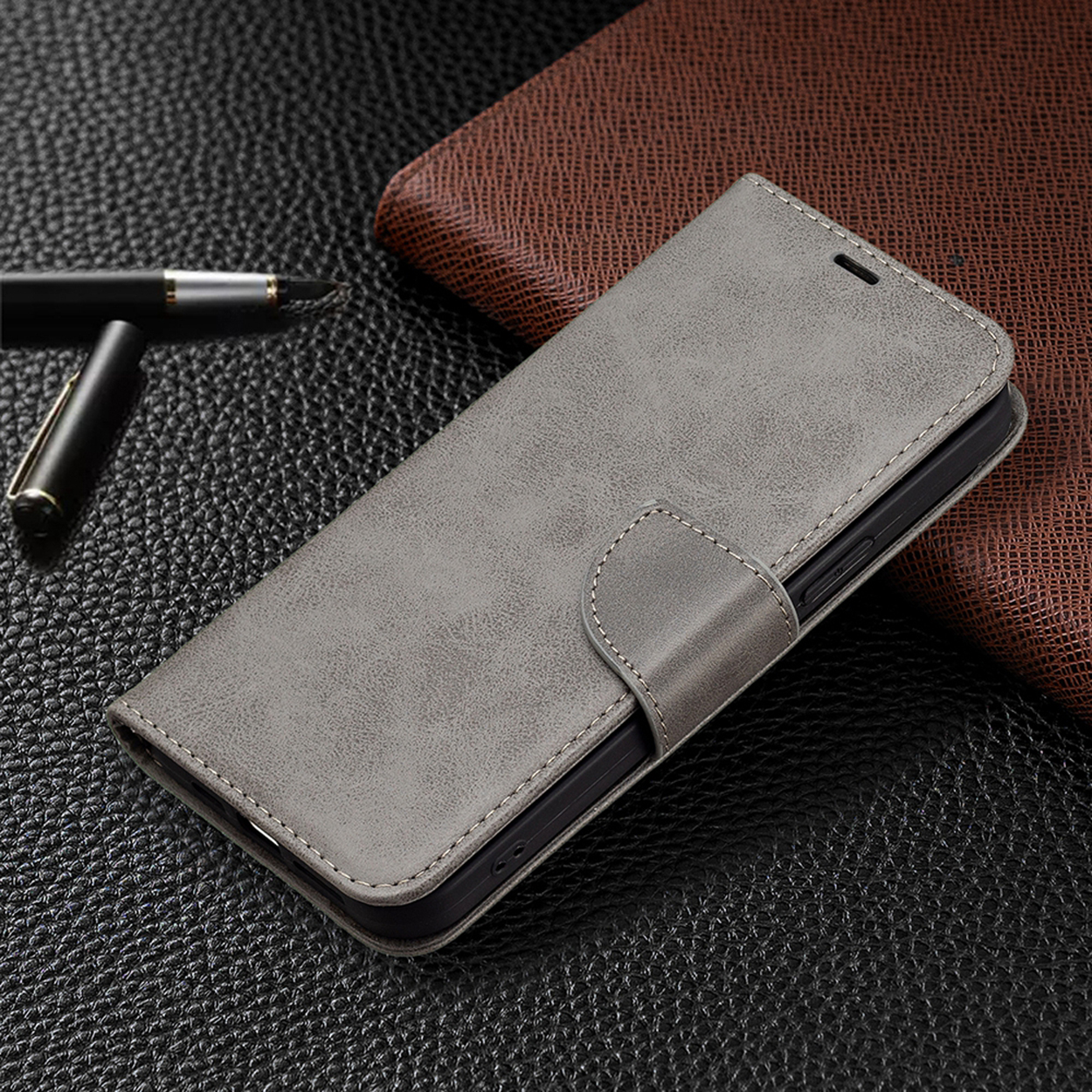 Grijze leren telefoonhoes met magneetsluiting, liggend op een gestructureerd zwart en bruin oppervlak.