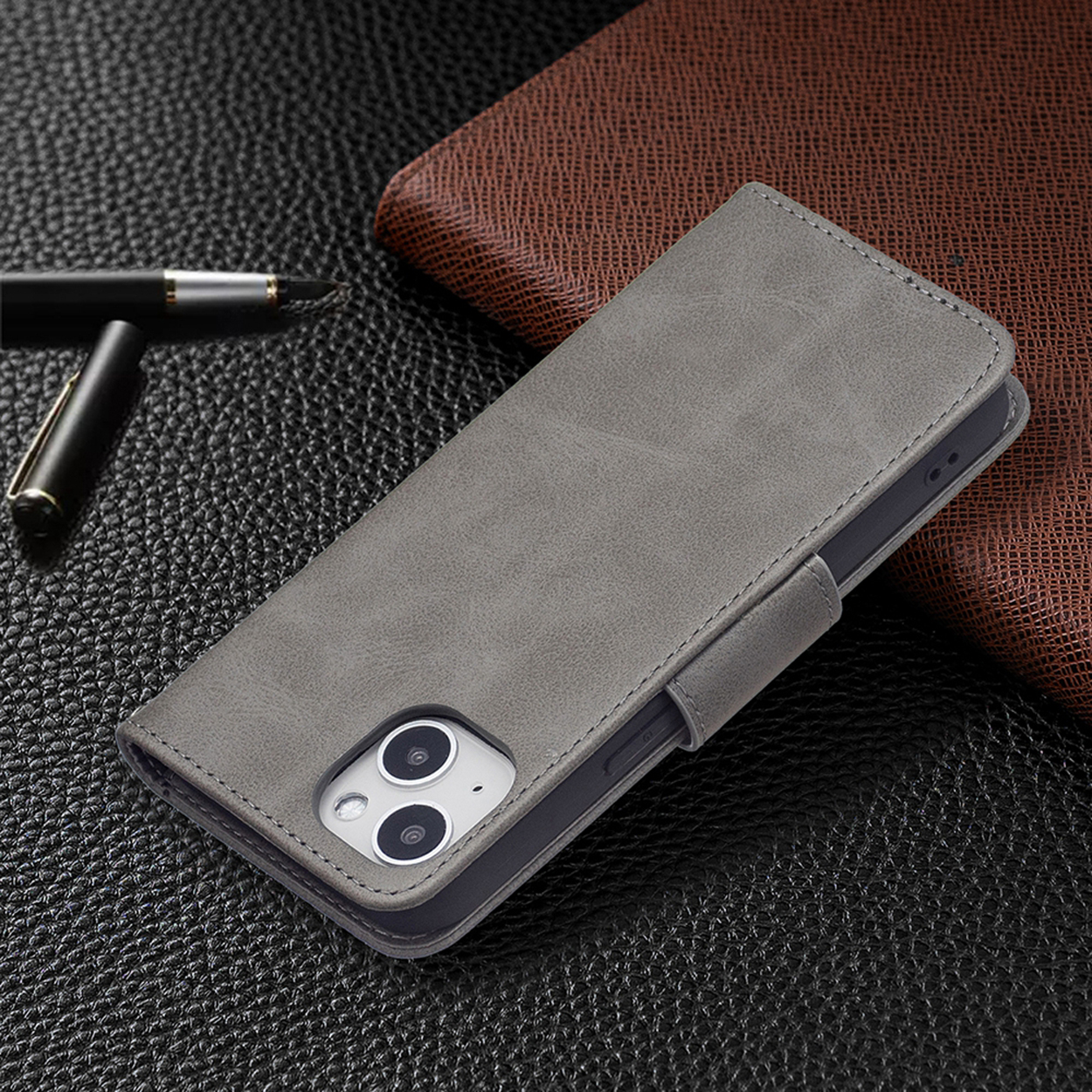Een grijze leren telefoonhoes op een zwart-bruin oppervlak. Er ligt ook een pen op het oppervlak.