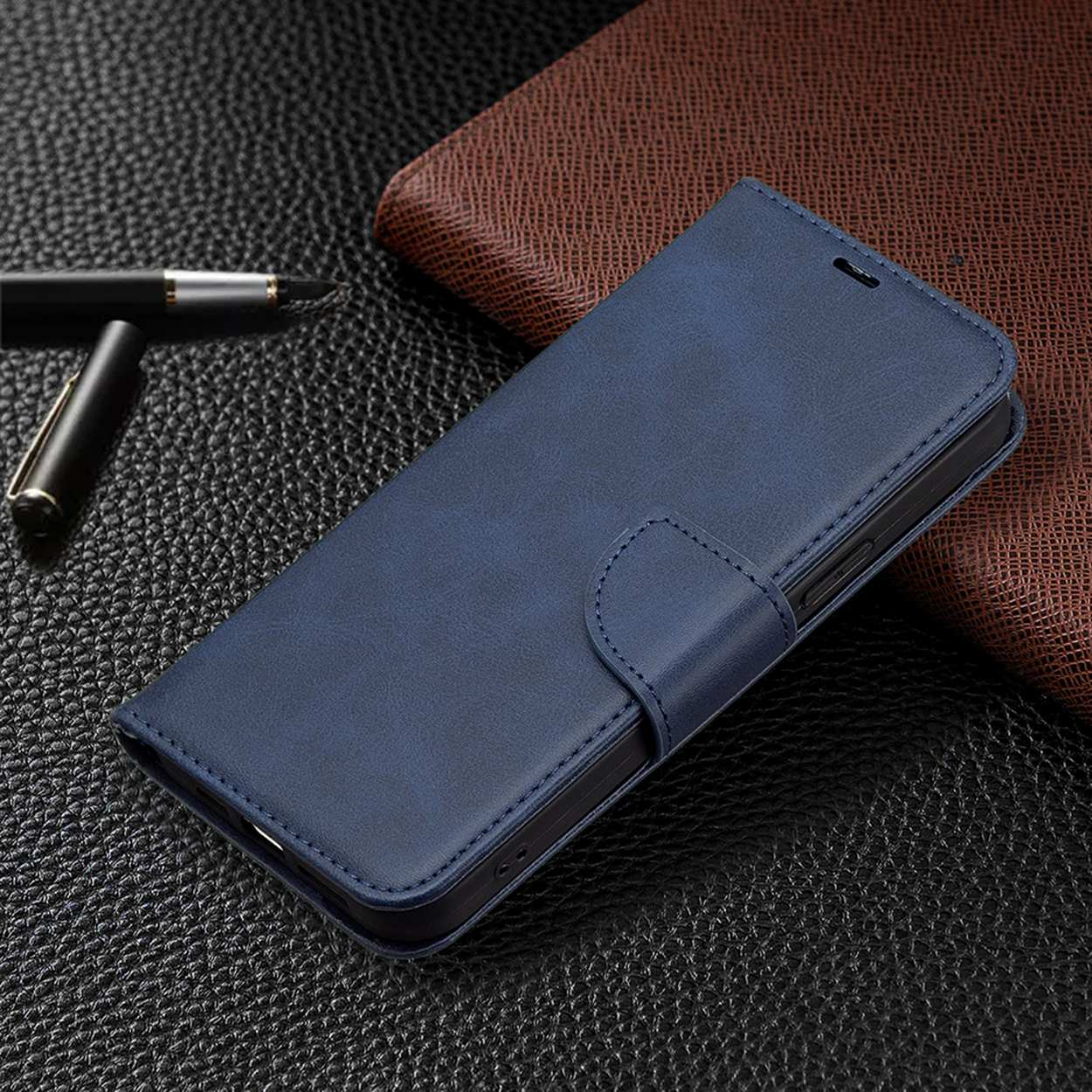 Blauwe leren telefoonhoes met een magnetische sluiting, op een getextureerd oppervlak met een pen en een bruine portemonnee op de achtergrond.