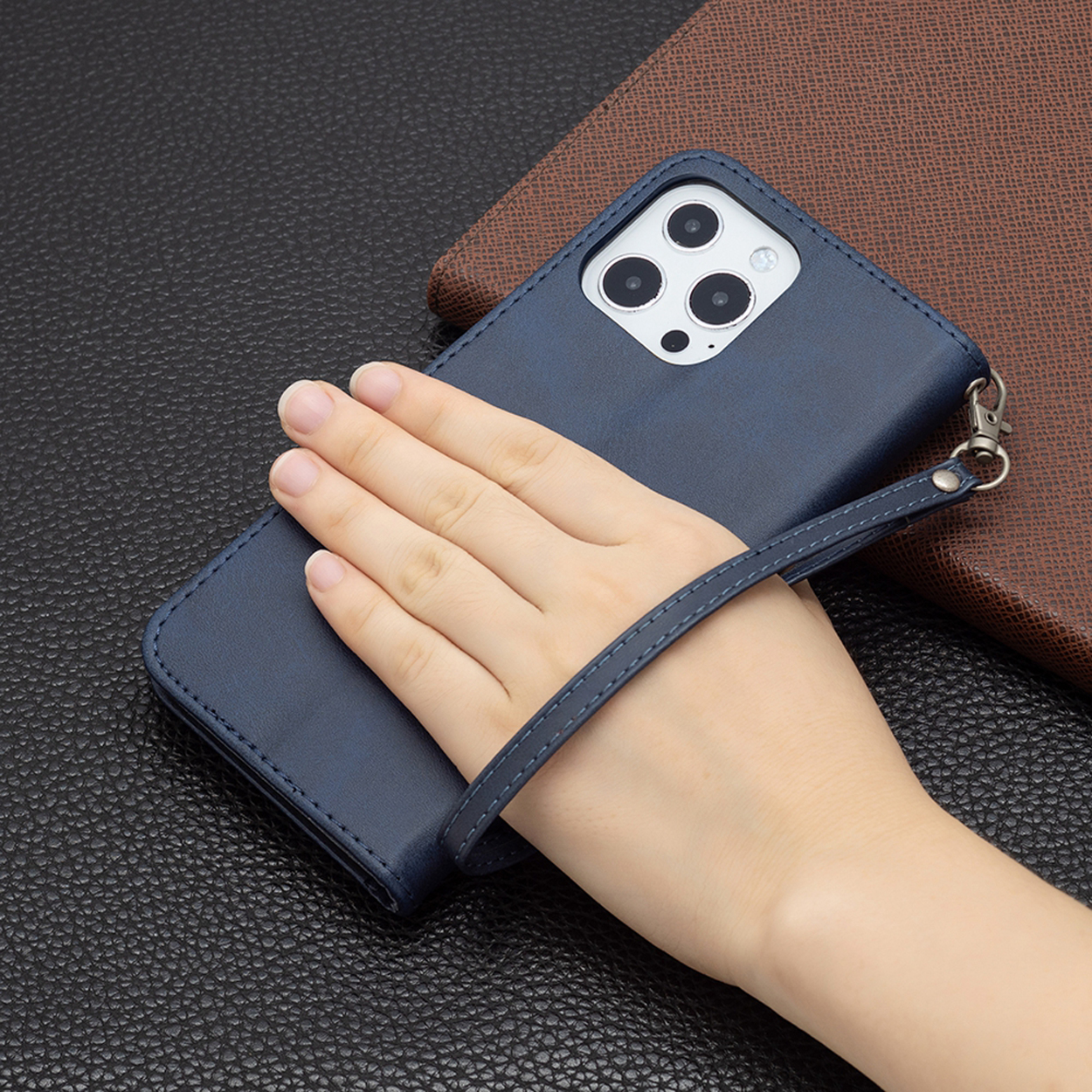 Hand die een donkerblauwe telefoonhoes met een riem vasthoudt. Een andere bruine hoes op de achtergrond.