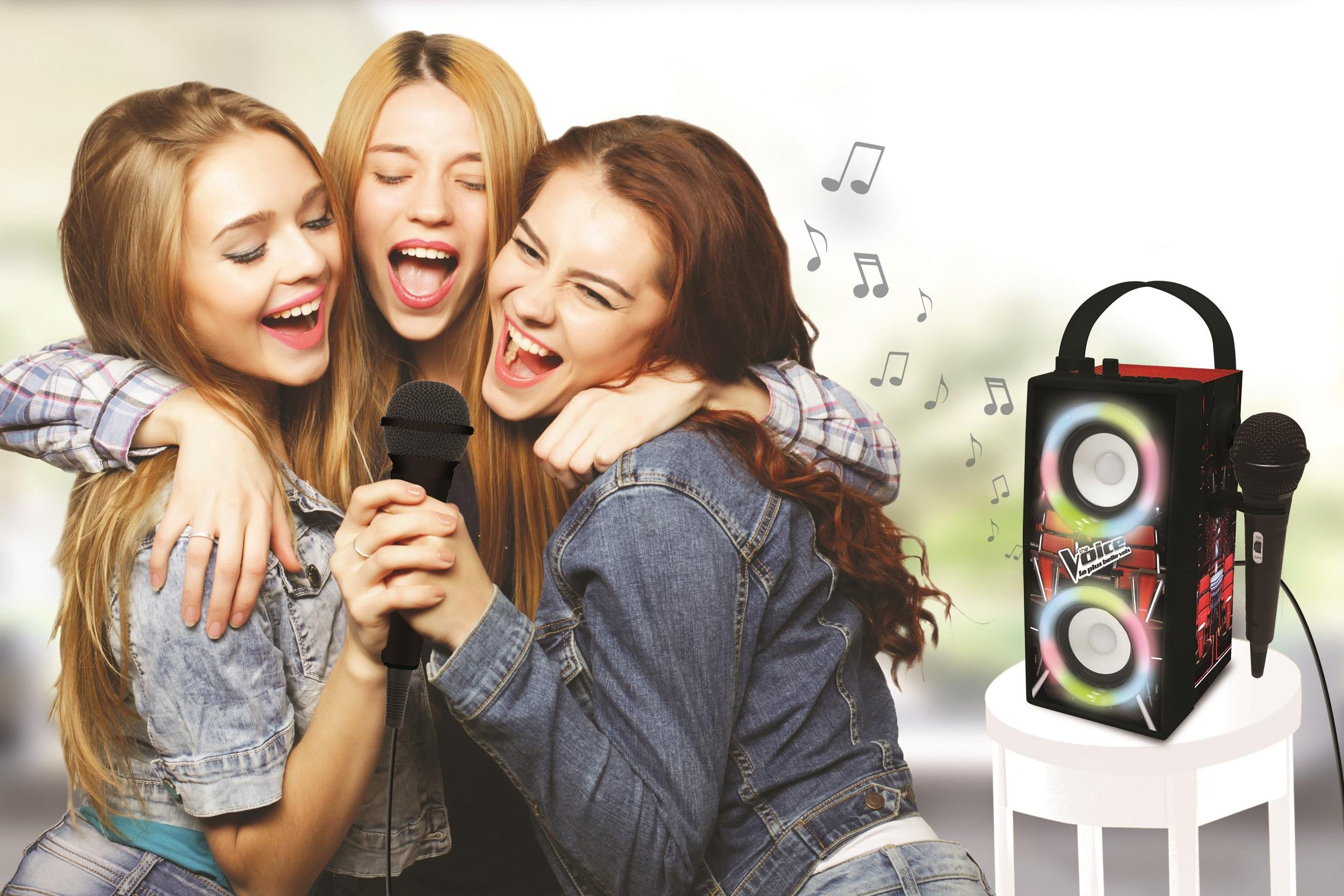 Tres mujeres cantando en micrófonos con una máquina de karaoke cerca.