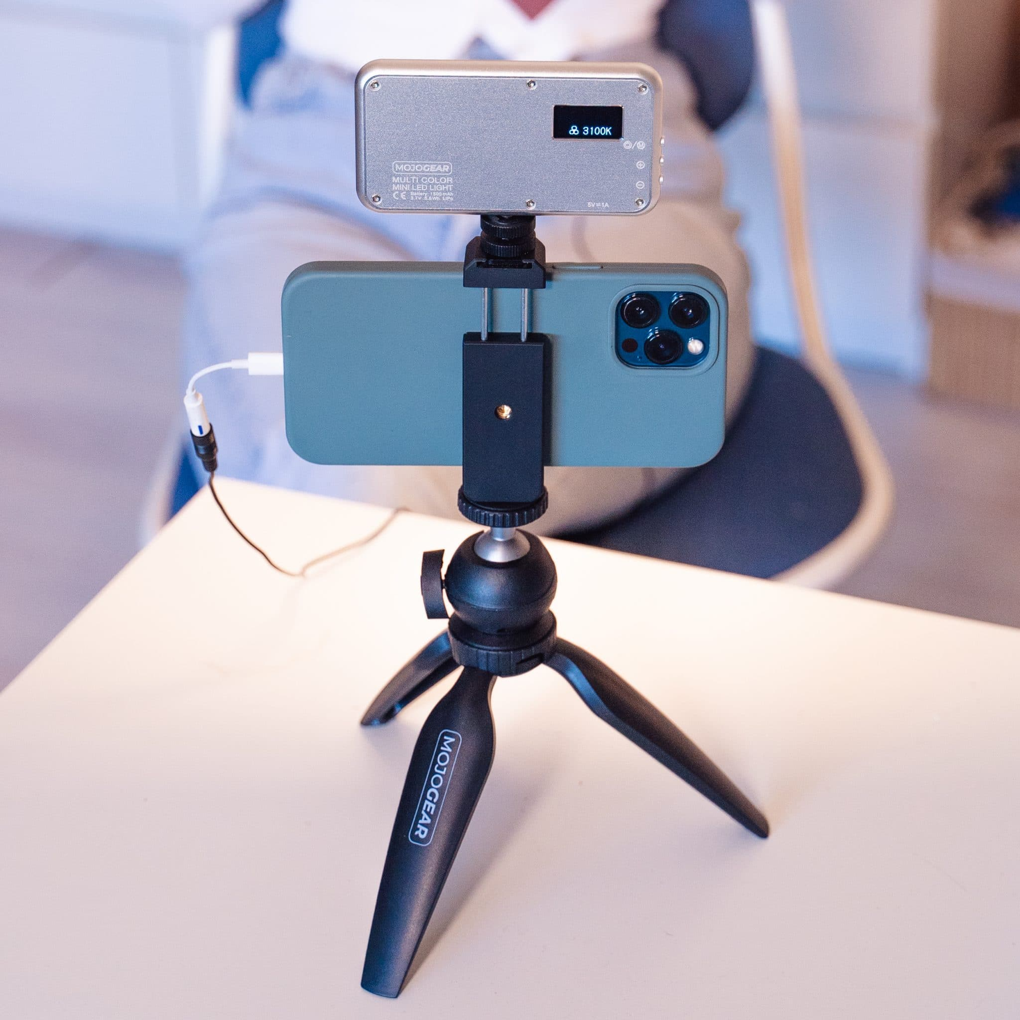 A phone mounted on a tripod with a light. A person is visible in the background.