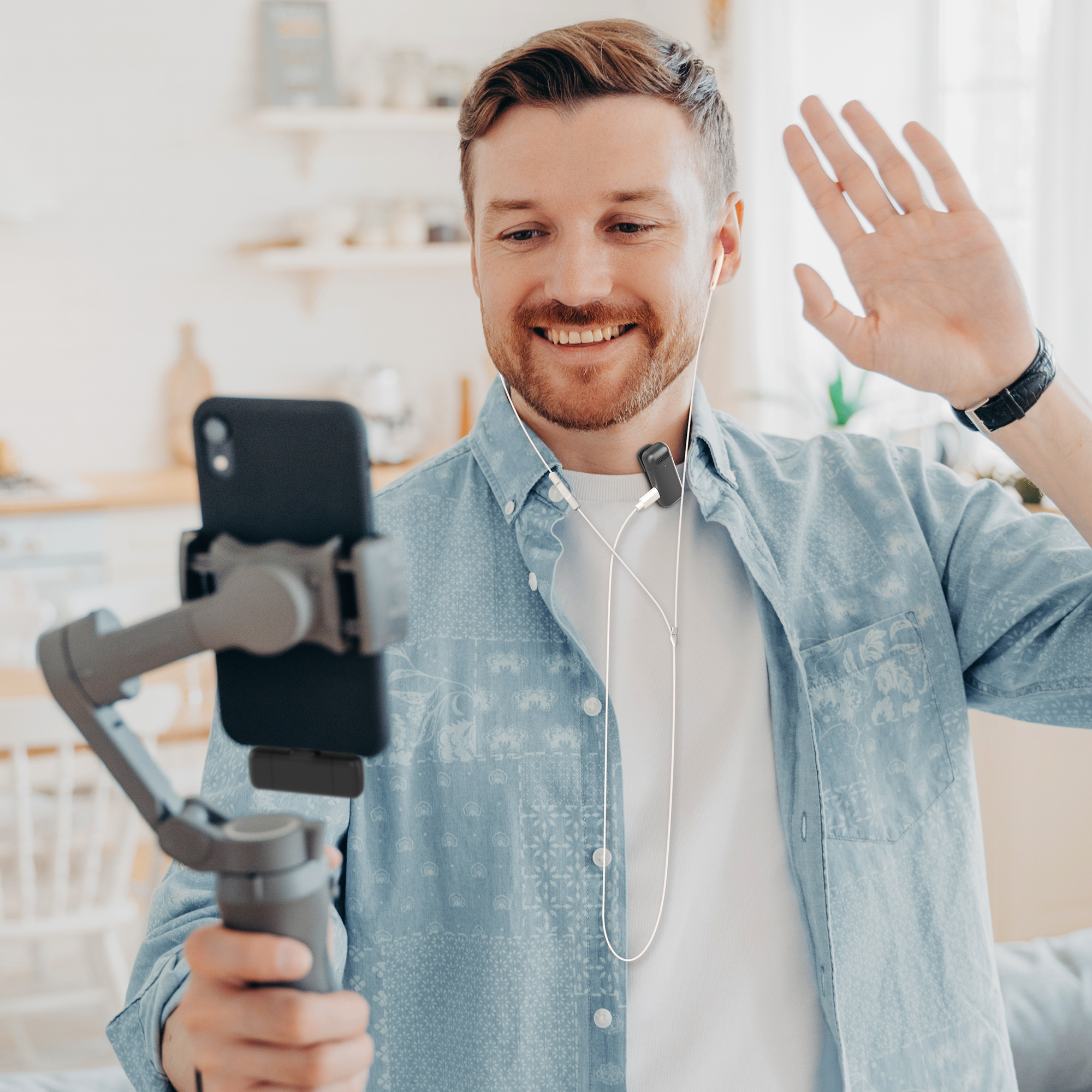 Man met baard zwaaiend, telefoon op een gimbal. Witte oortelefoons, binnen.