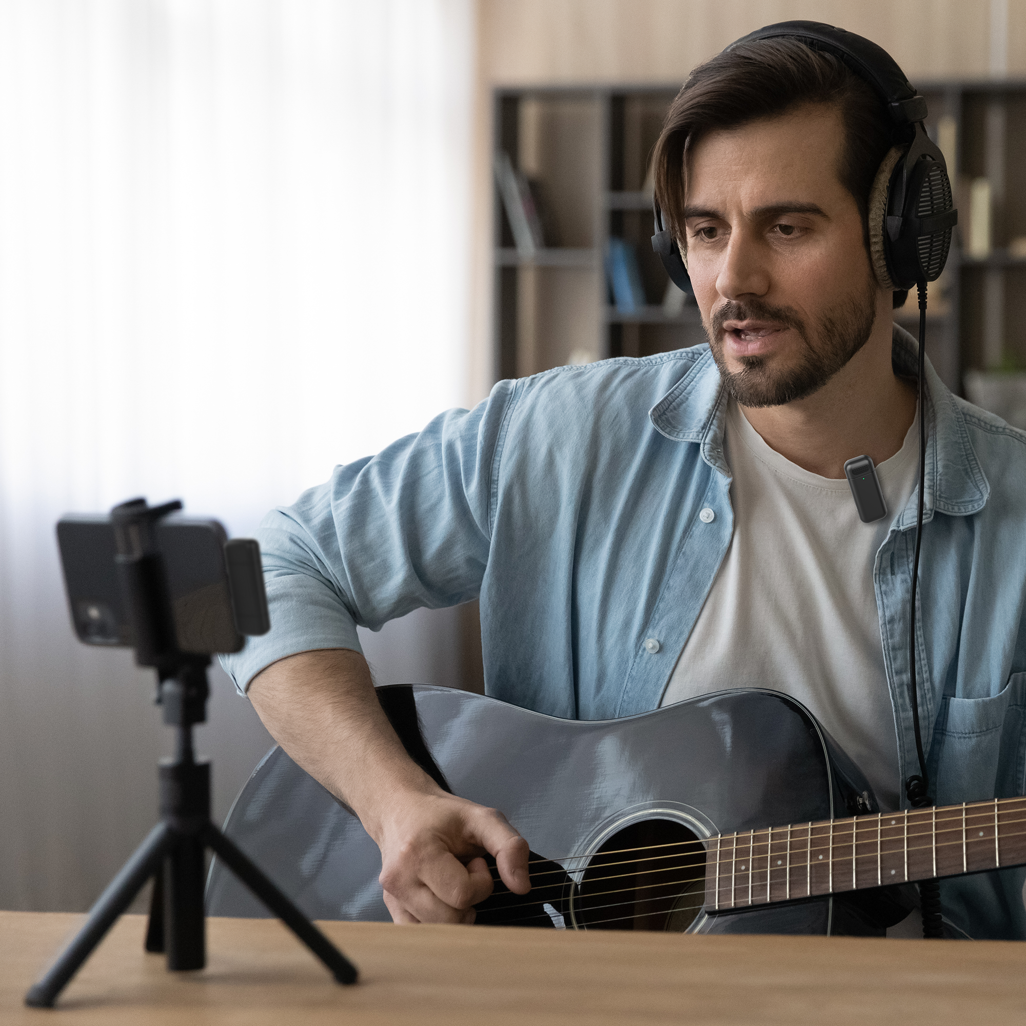 Man met koptelefoon, gitaar en telefoon op statief, die een muziekvideo opneemt.