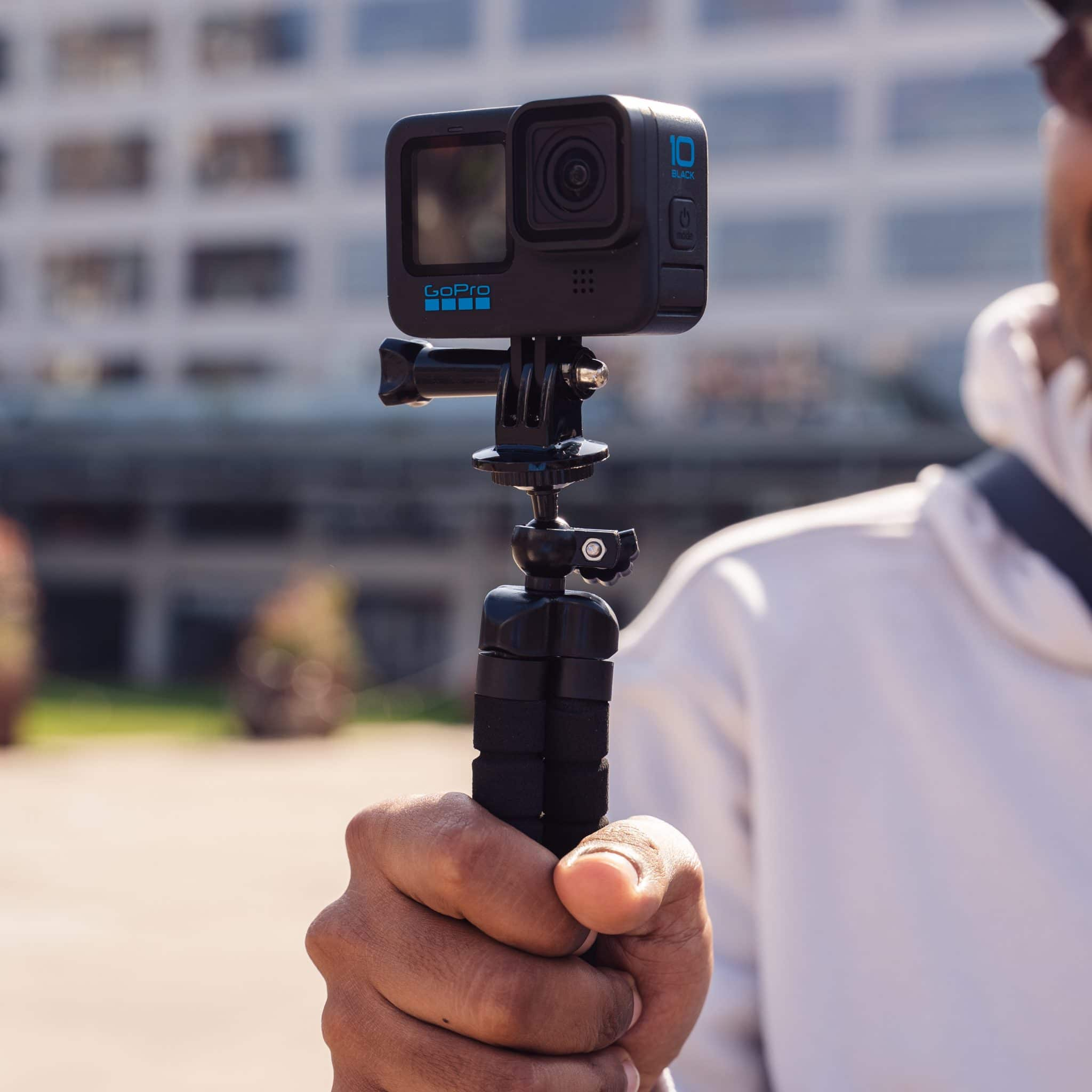 Een persoon houdt een GoPro-camera op een statief. De camera is zwart met een blauw GoPro-logo.