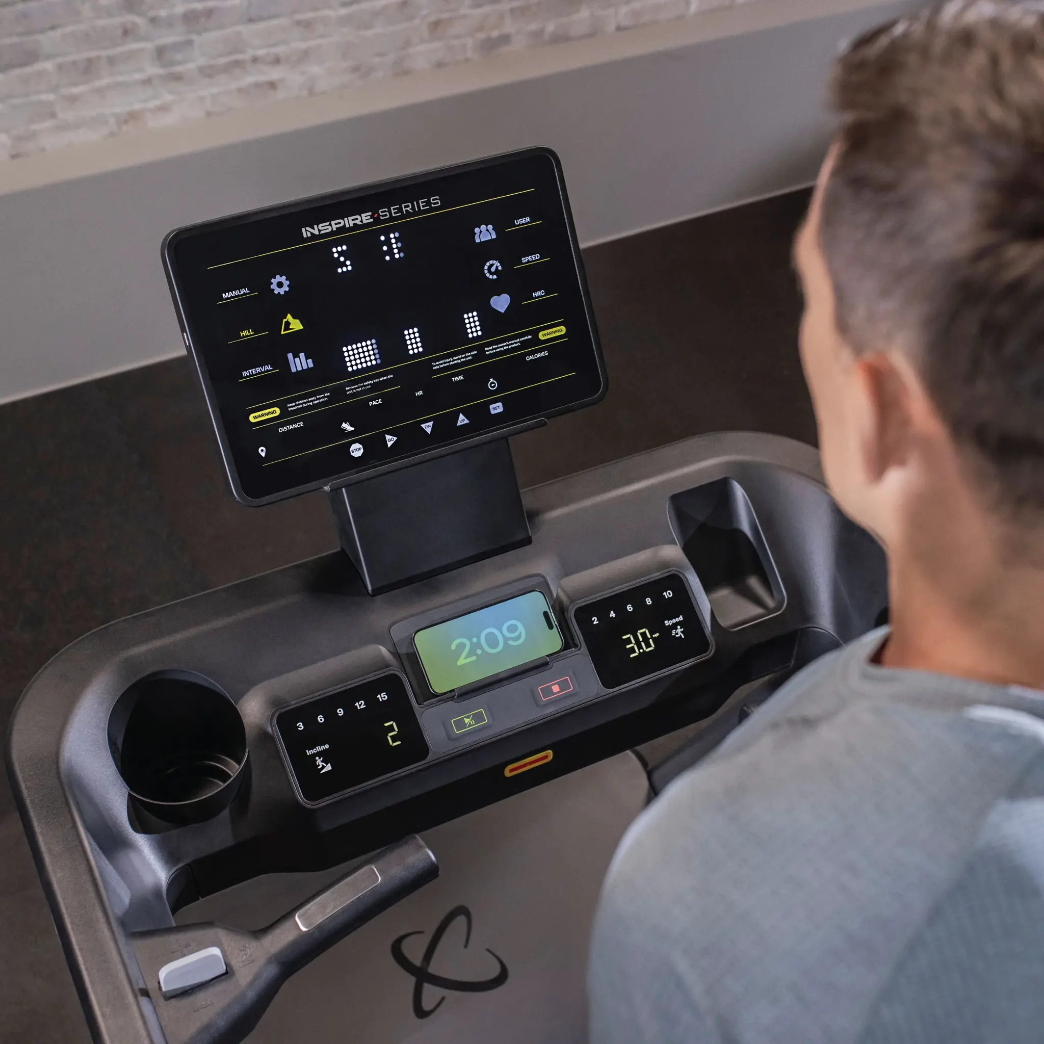 A person on a treadmill with display showing exercise data. Black and grey color scheme.