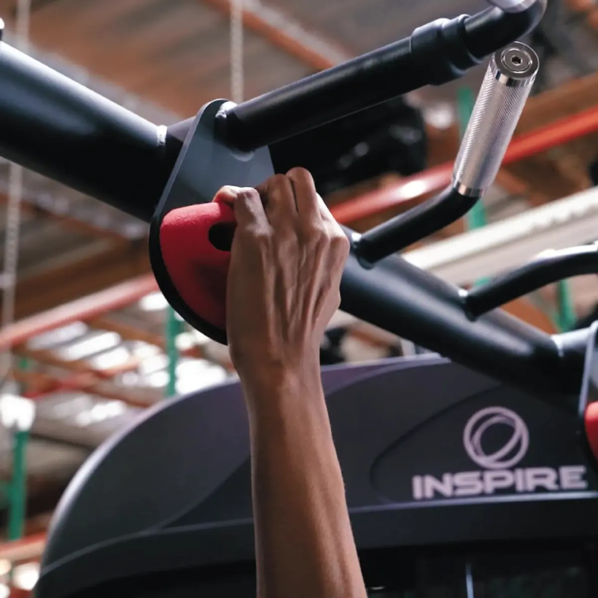 De hand van een persoon die een rode greep op een fitnessapparaat vasthoudt.