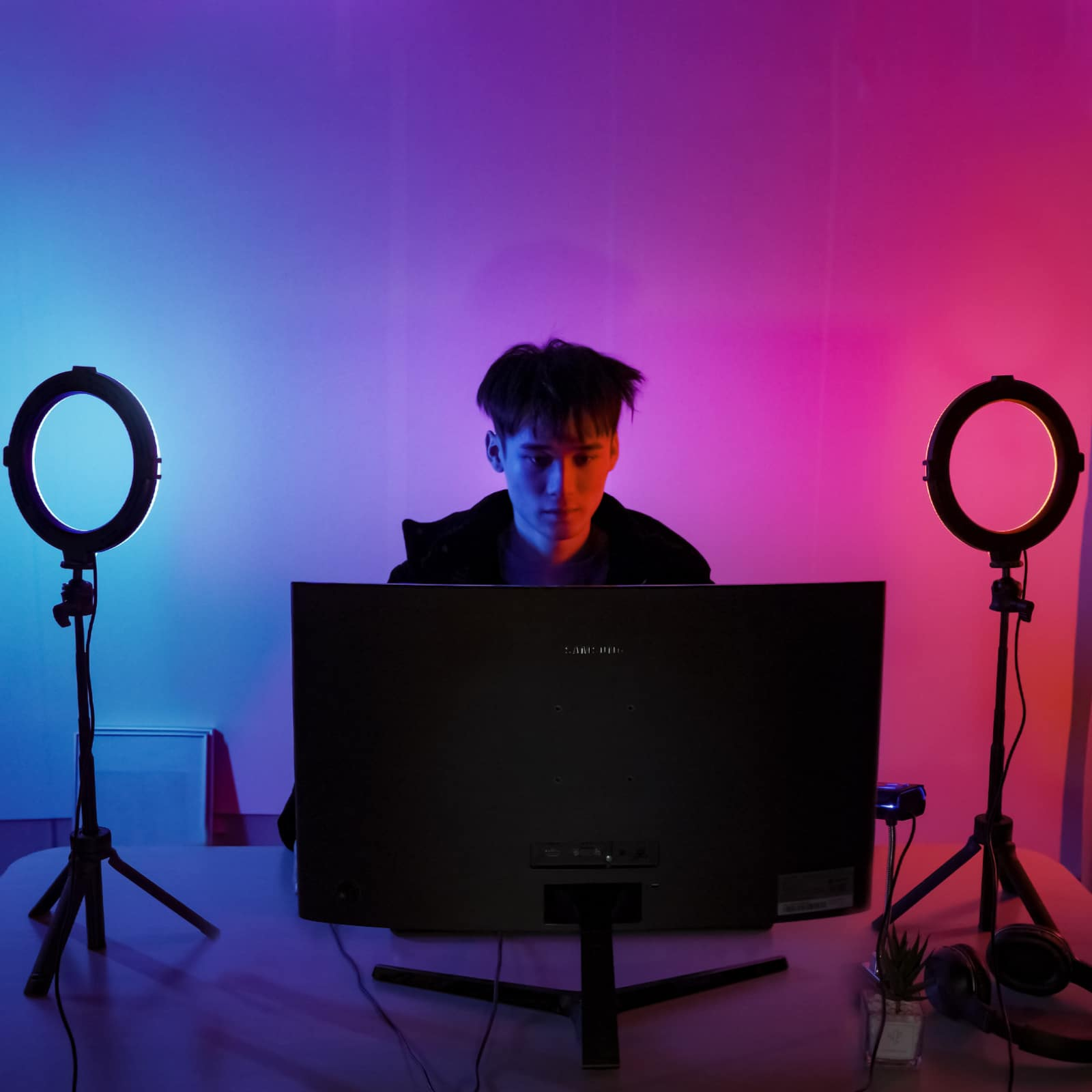 A man is in front of a computer monitor, with two ring lights. The background is colorful.
