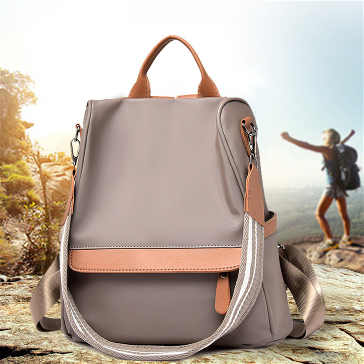 Ein grauer Rucksack mit braunem Riemen und eine Person, die im Hintergrund an einem sonnigen Tag wandert.