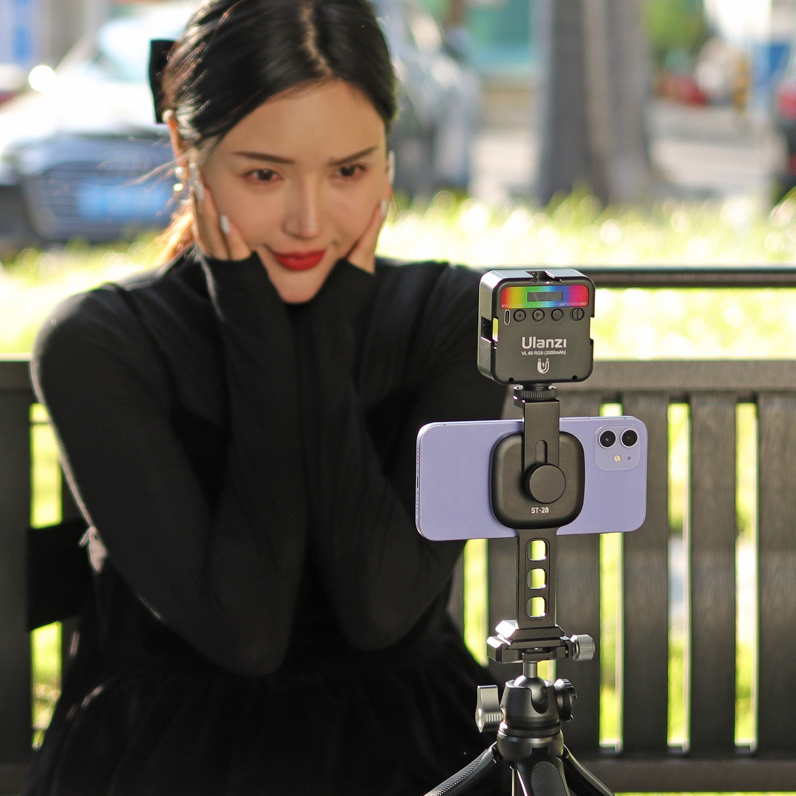A woman holding her face, looking at a phone mounted on a tripod with a light.