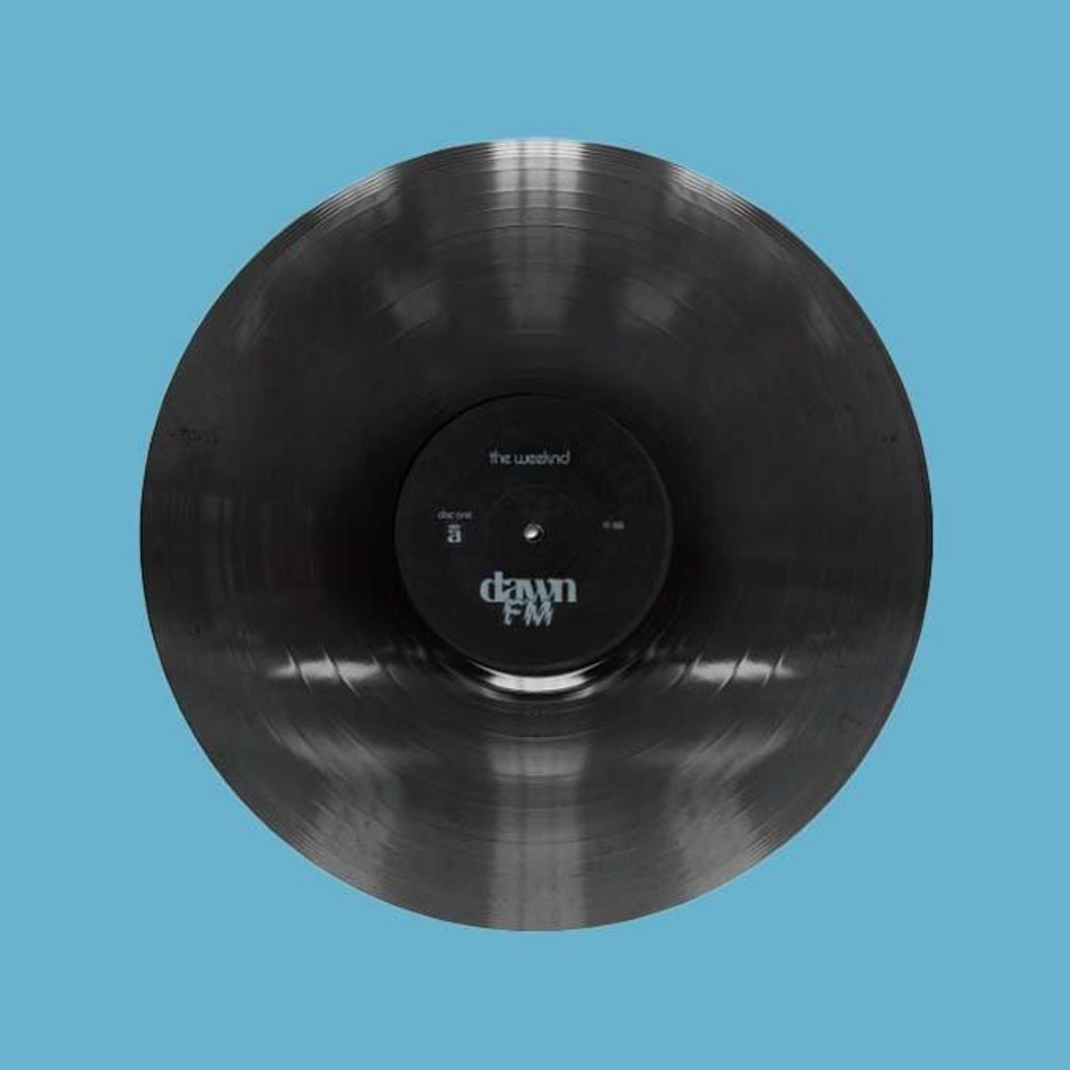 Vinile nero con etichetta, 'Dawn FM' di The Weeknd, su sfondo blu.