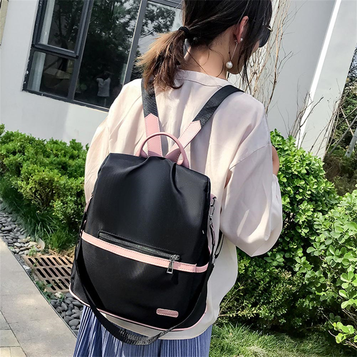 Frau mit schwarzem Rucksack mit rosa Akzenten, steht draußen in der Nähe von Grün.