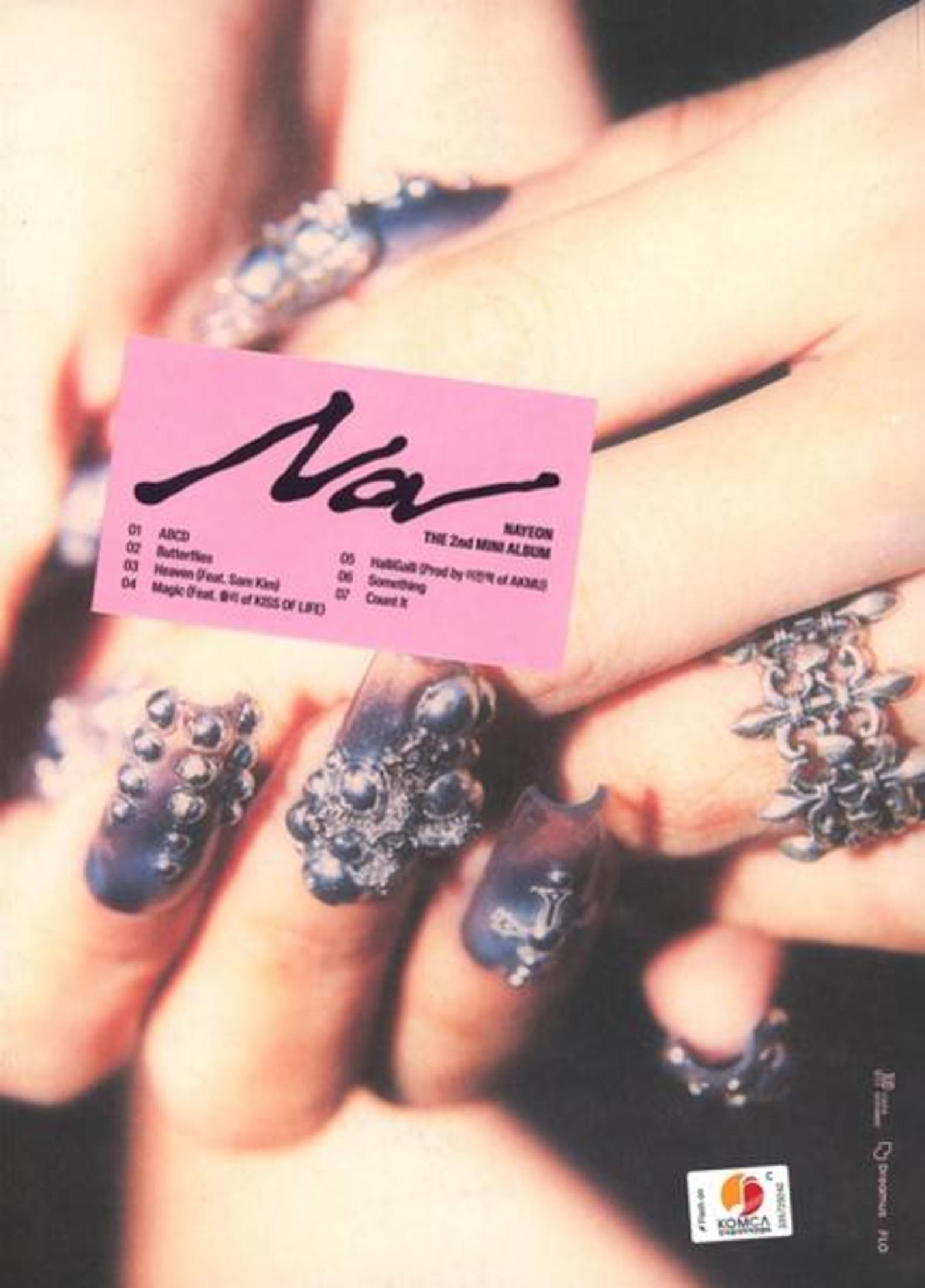 Close-up of hands with elaborate nail art, pink album cover in the background.