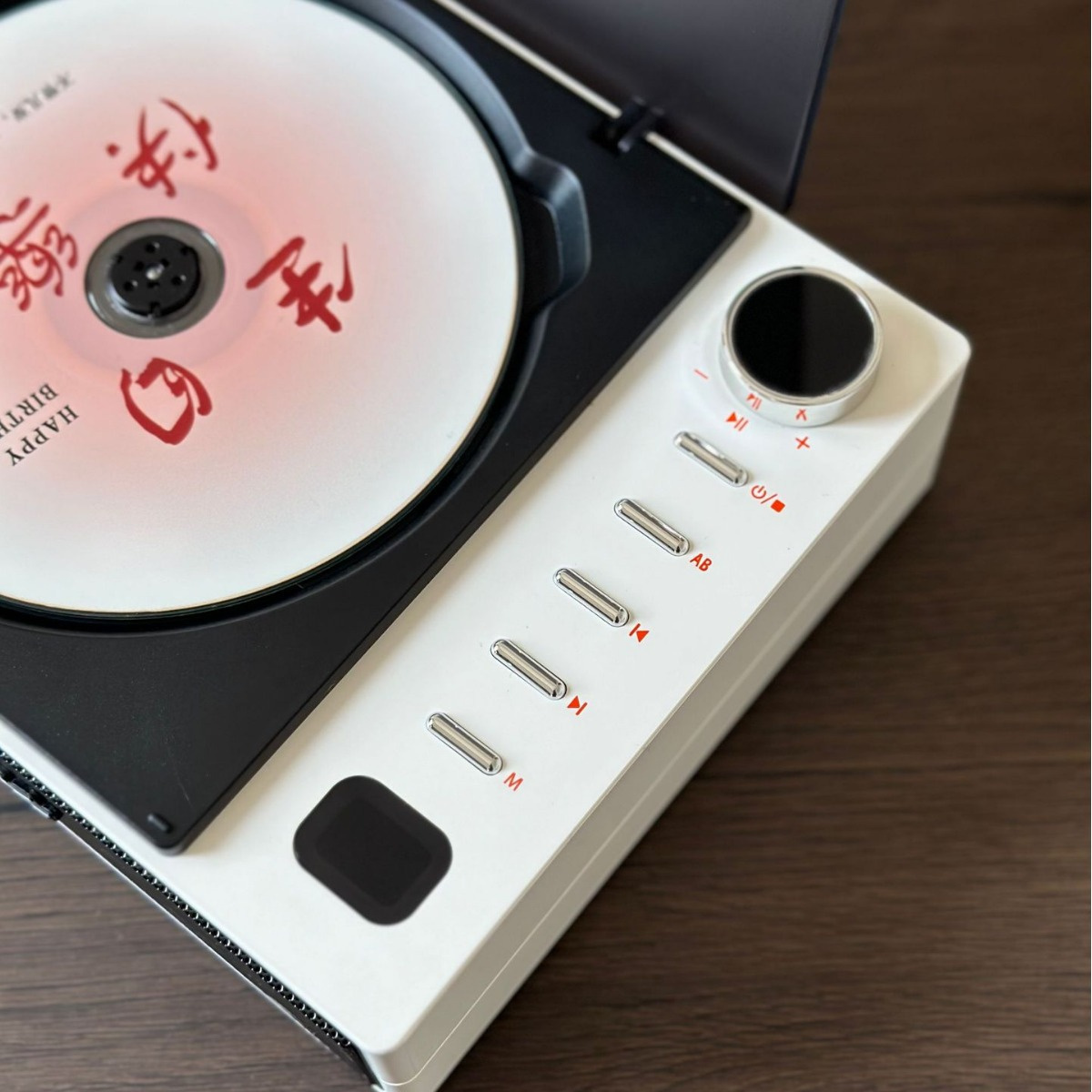 Weiß-schwarzer CD-Player mit CD. Knöpfe und ein Drehknopf sind sichtbar. Holzoberfläche.