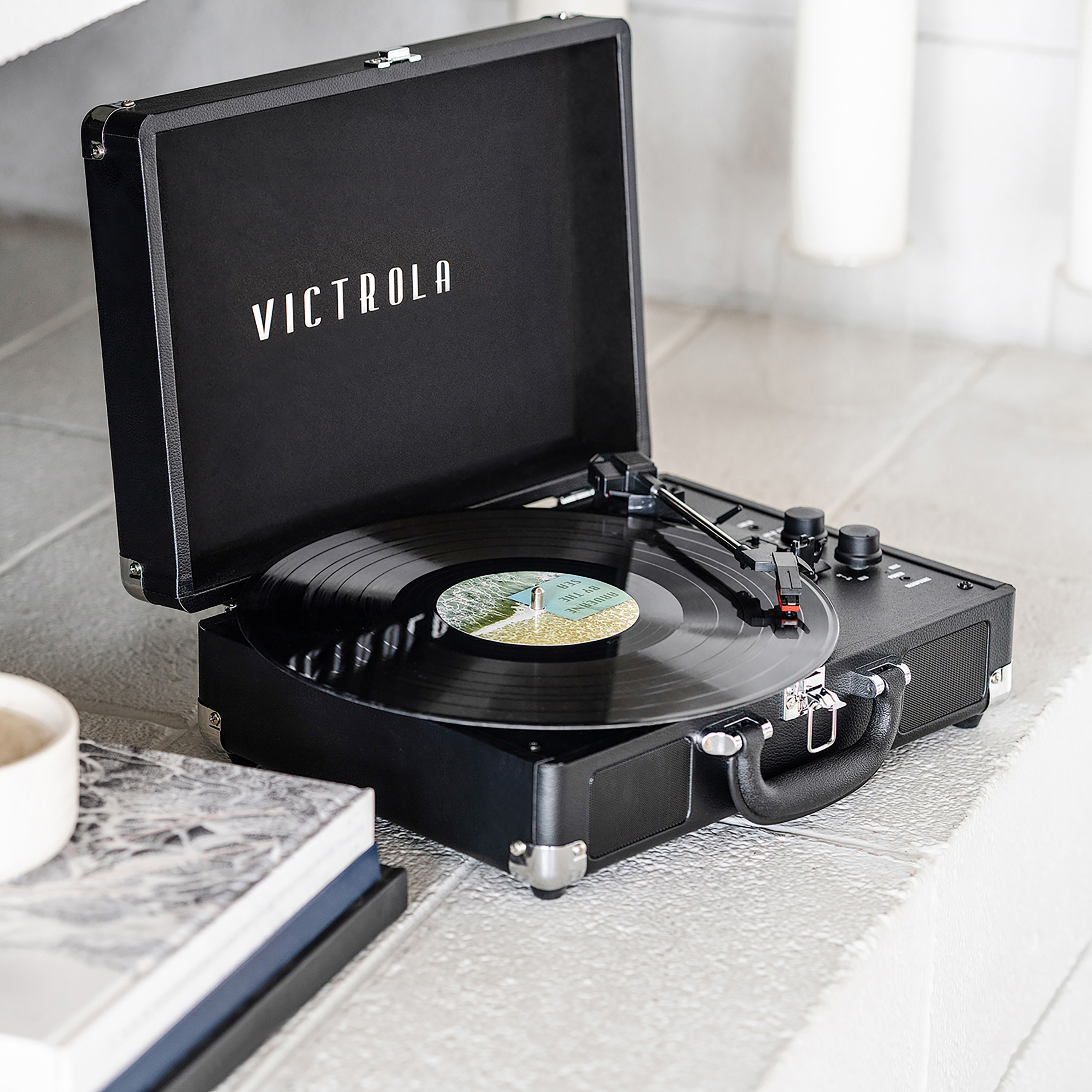 Tocadiscos Victrola negro con disco en reproducción. Fondo blanco.
