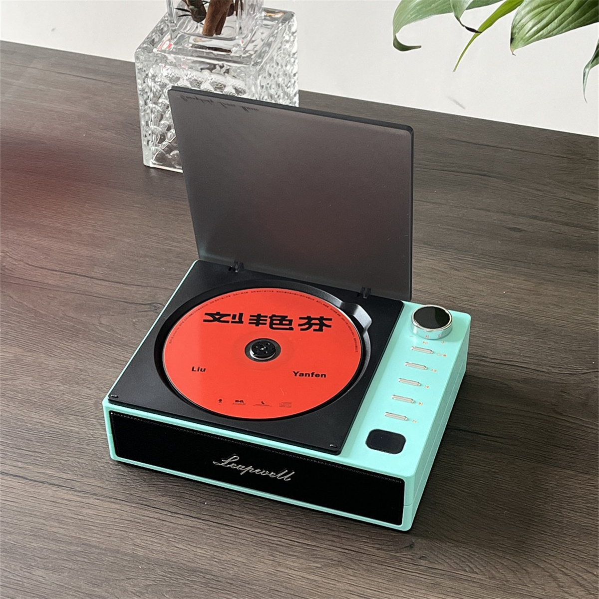 Plattenspieler mit roter CD. Schwarz und mintgrün, offener Deckel, auf einem Holztisch.
