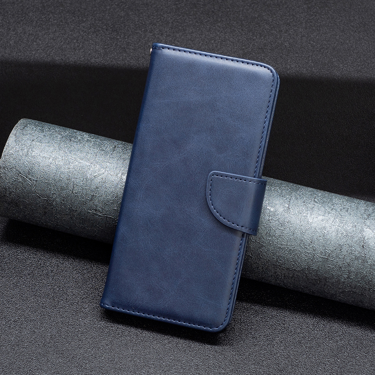 Een blauwe leren telefoonhoes, gesloten en met een magnetische sluiting. Het ligt op een donker, getextureerd oppervlak.