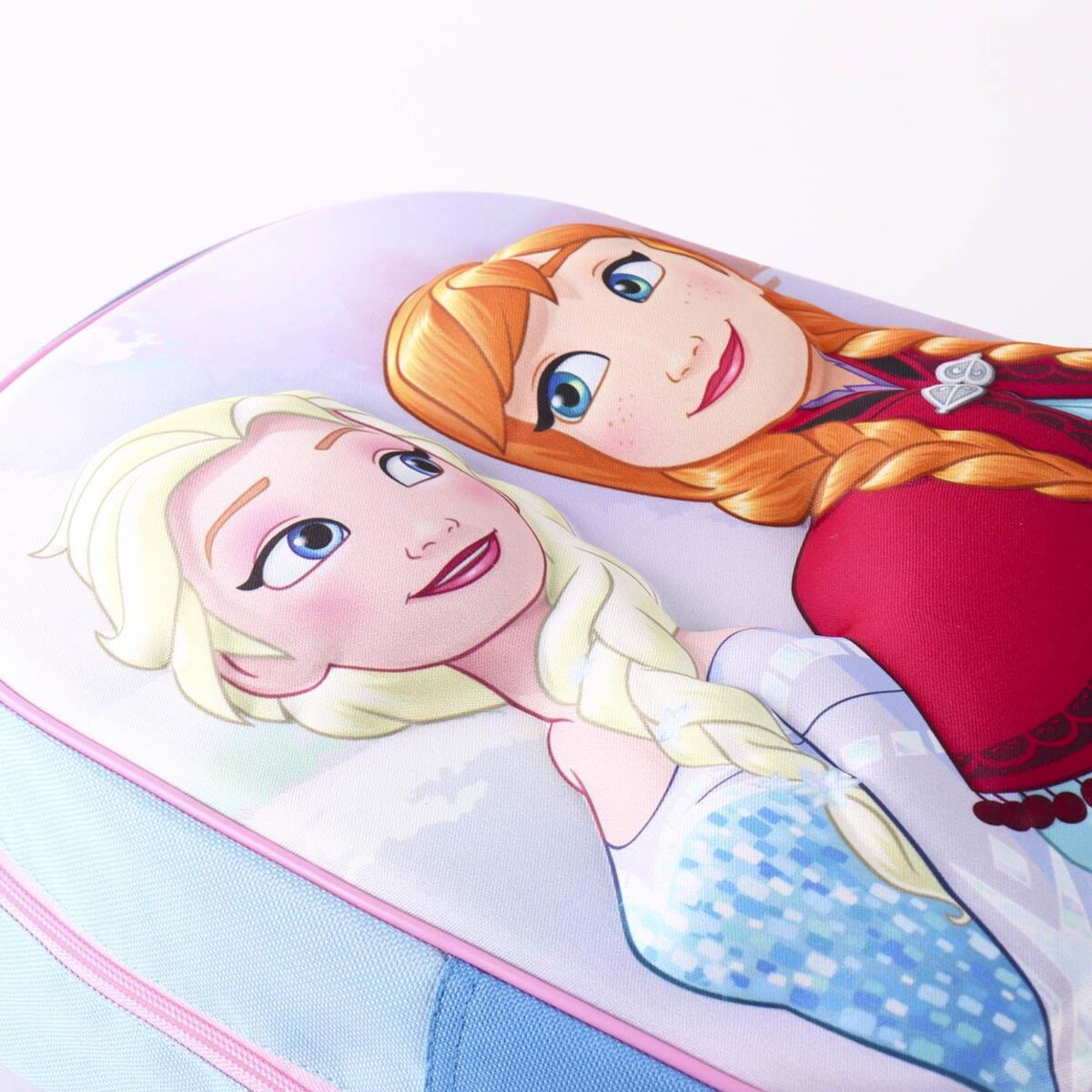 Primer plano de Anna y Elsa de Frozen en una mochila azul. Anna tiene cabello rojo, Elsa rubio. Cremallera rosa y correas azules.