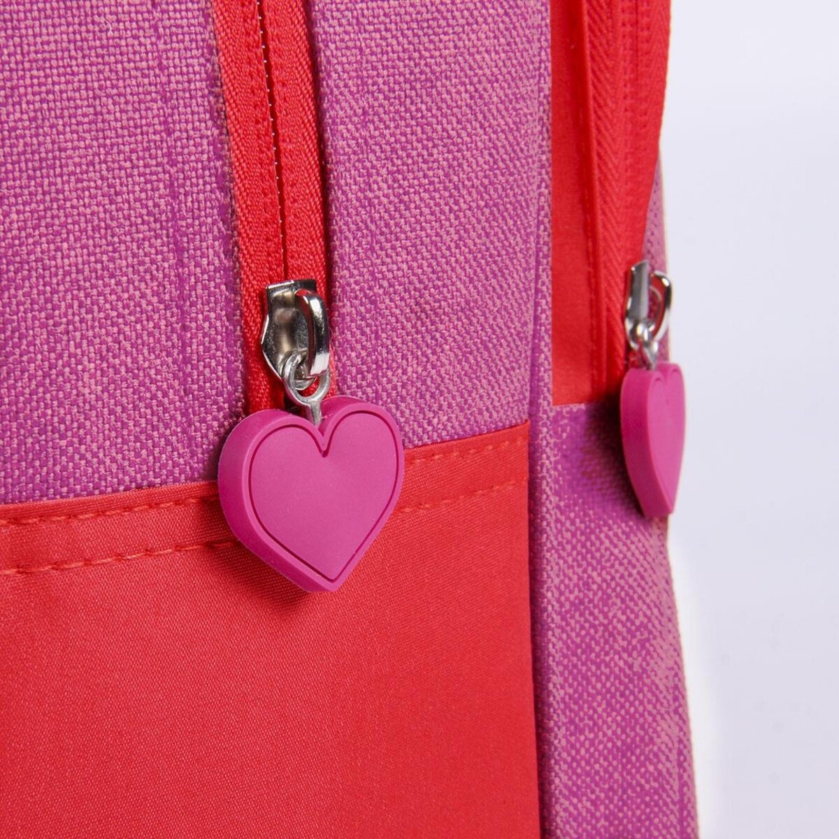 Primer plano de tiradores de cremallera en forma de corazón en una mochila roja y rosa de Peppa Pig.