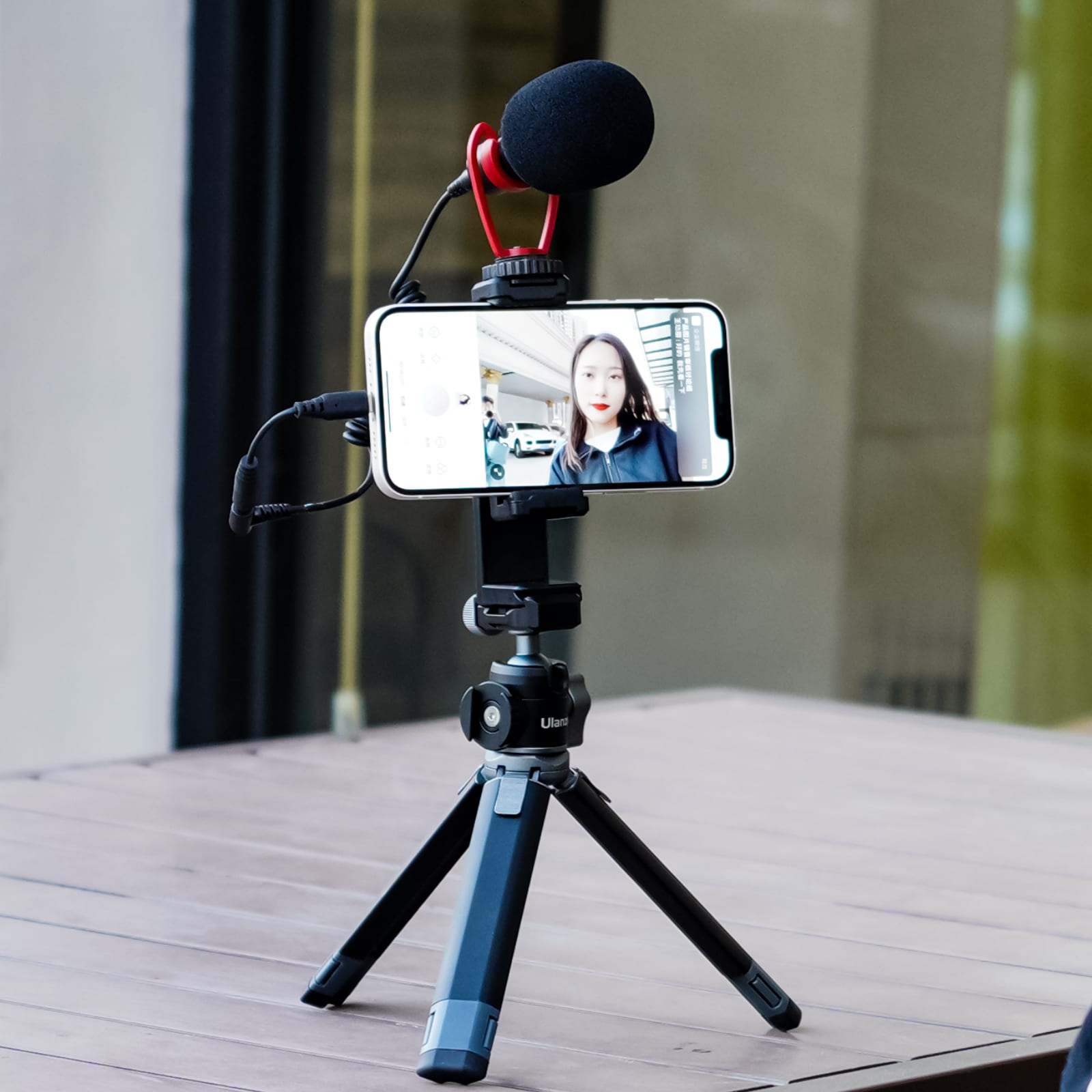 Un smartphone avec une personne à l'écran, micro attaché, sur trépied, à l'extérieur.