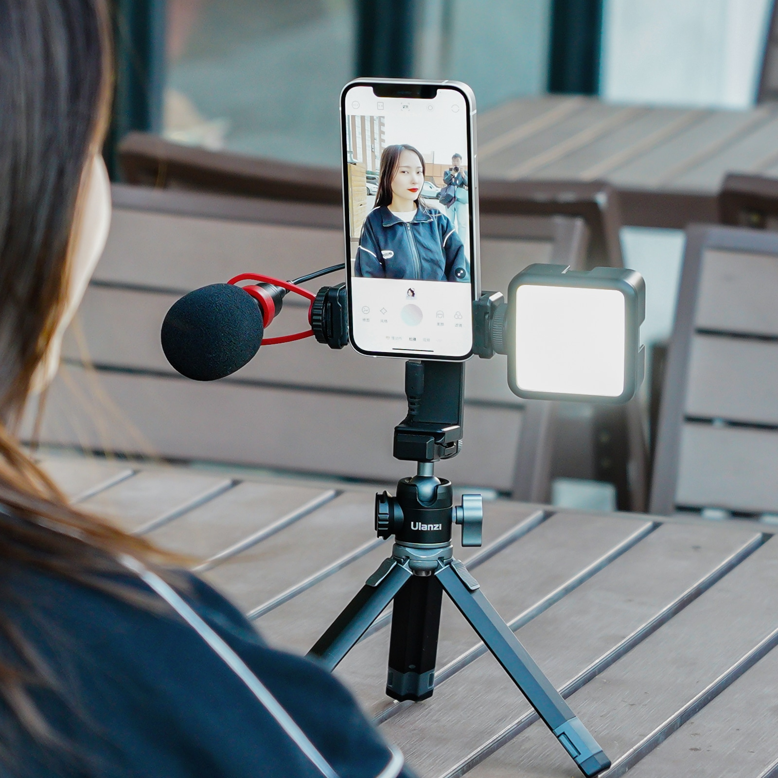 Une femme filme avec un smartphone et un microphone sur un trépied, avec une lumière.