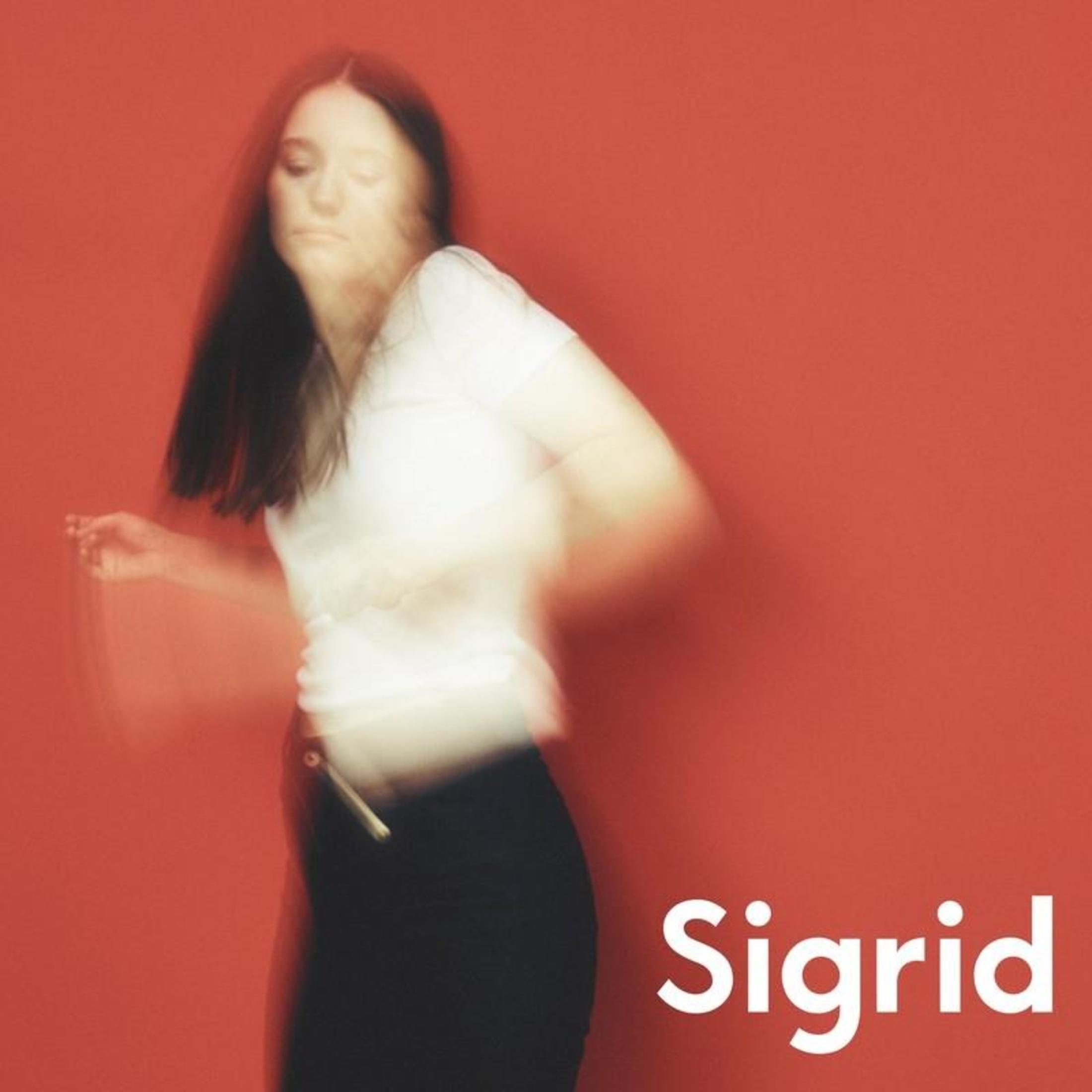 Immagine sfocata di una donna con maglietta bianca e pantaloni neri su sfondo rosso. Scritto 'Sigrid'.