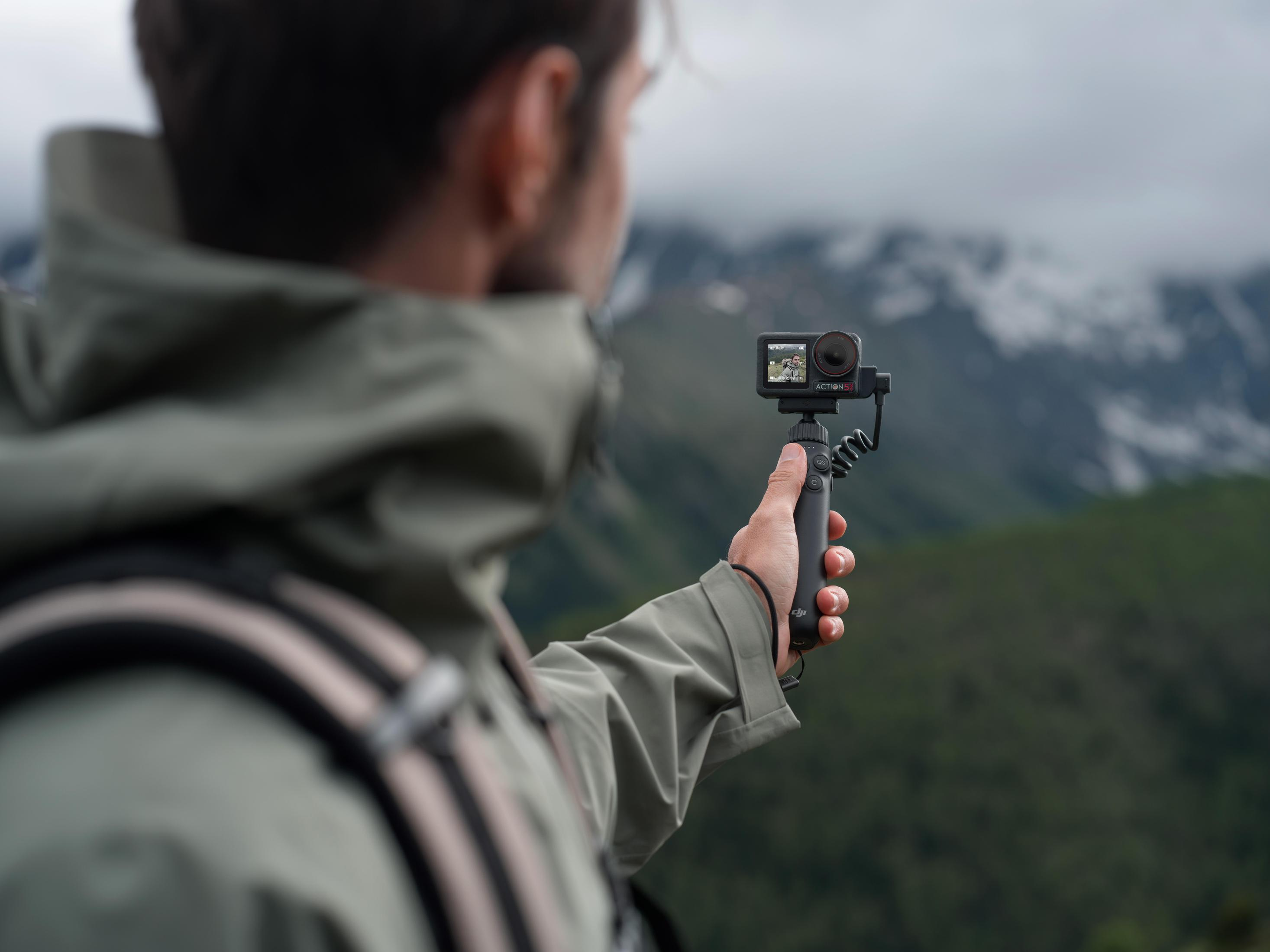 Uomo che tiene una action camera, riprendendo un paesaggio montano.