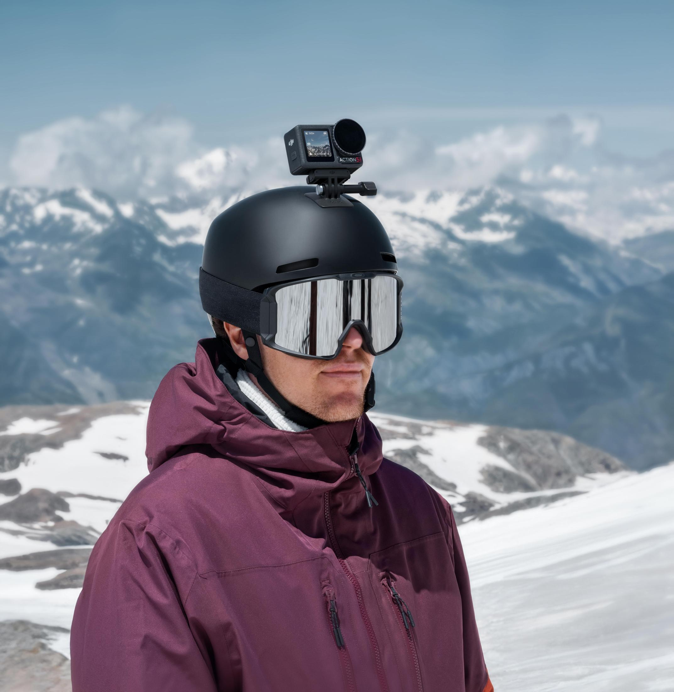 Eine Person mit einem schwarzen Skihelm und einer Brille mit einer Kamera. Schneeberg-Hintergrund.