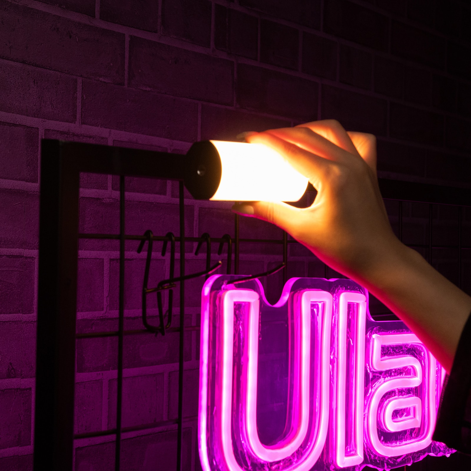 Ręka trzymająca cylindryczne światło na tle fioletowej ceglanej ściany i neonu.