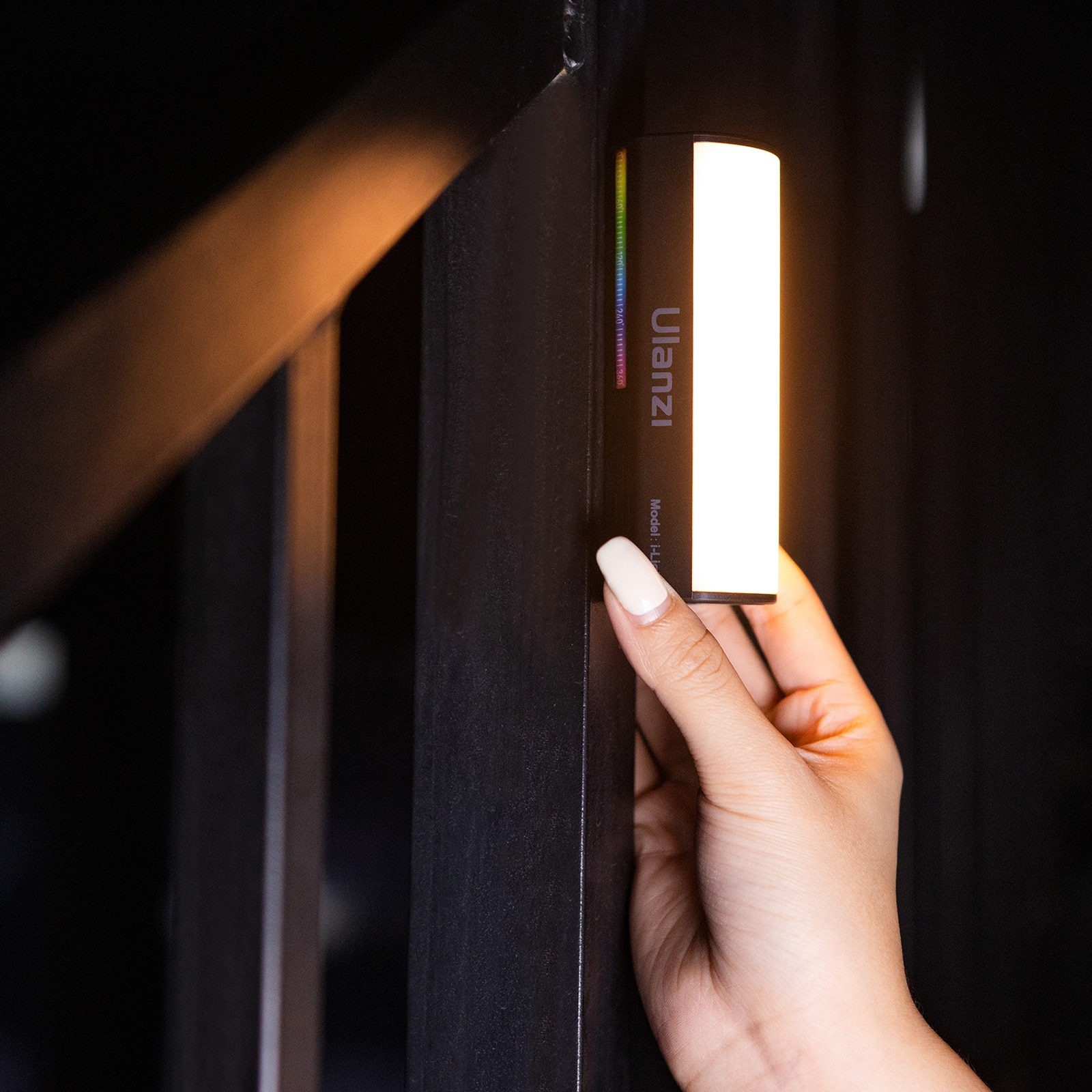 Dłoń trzymająca listwę świetlną LED Ulanzi na czarnej metalowej konstrukcji w ciemnym otoczeniu.