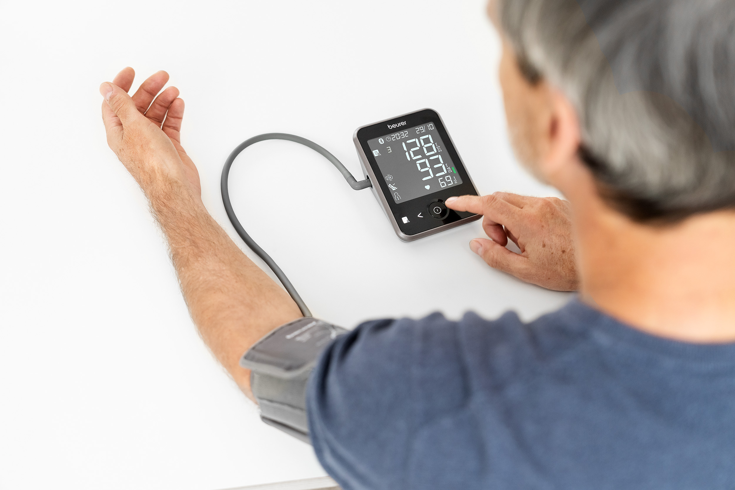 Man using blood pressure monitor. Display shows readings. He has the cuff on his arm.
