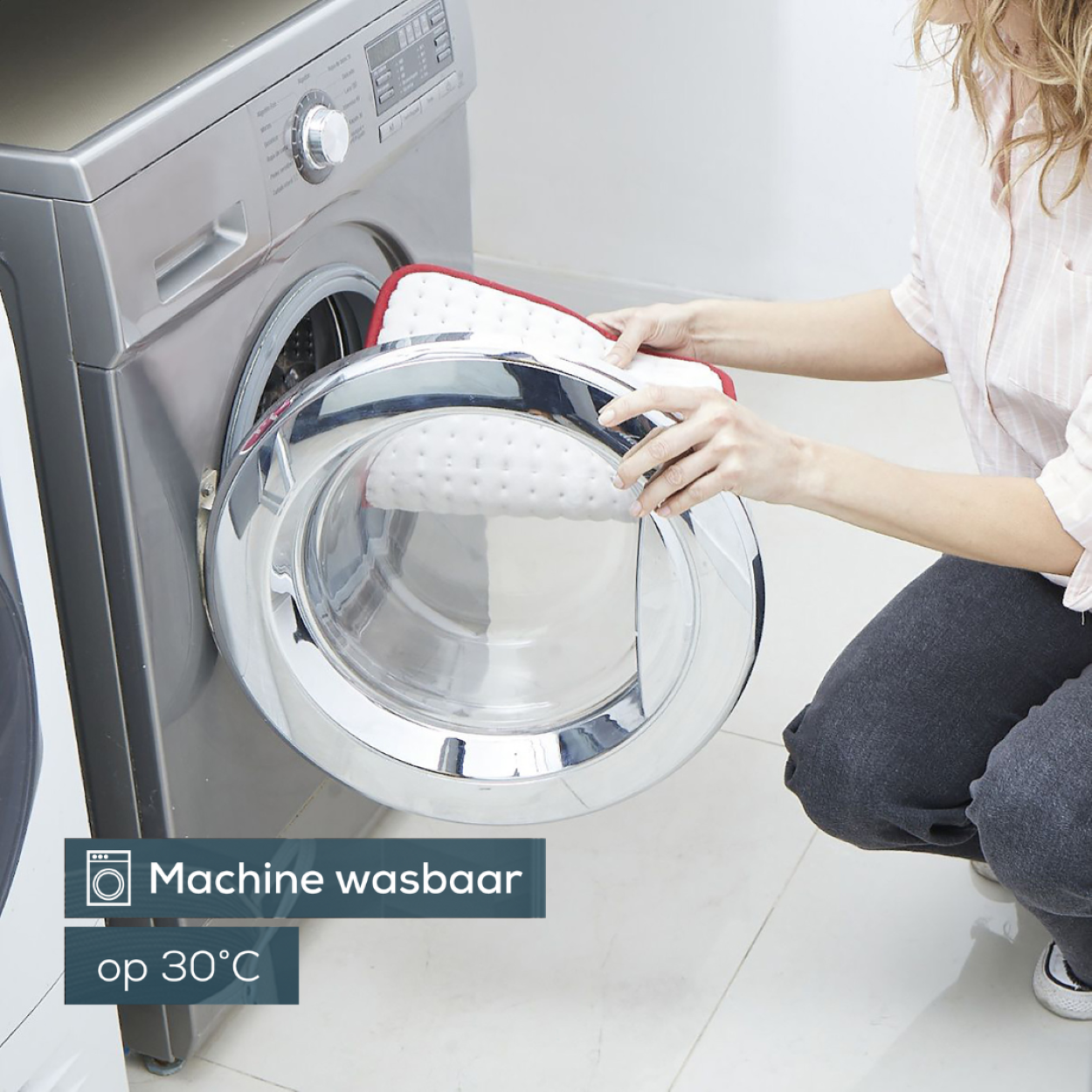 Una donna mette un cuscinetto bianco e rosso in lavatrice. Testo: Lavabile in lavatrice a 30°C.