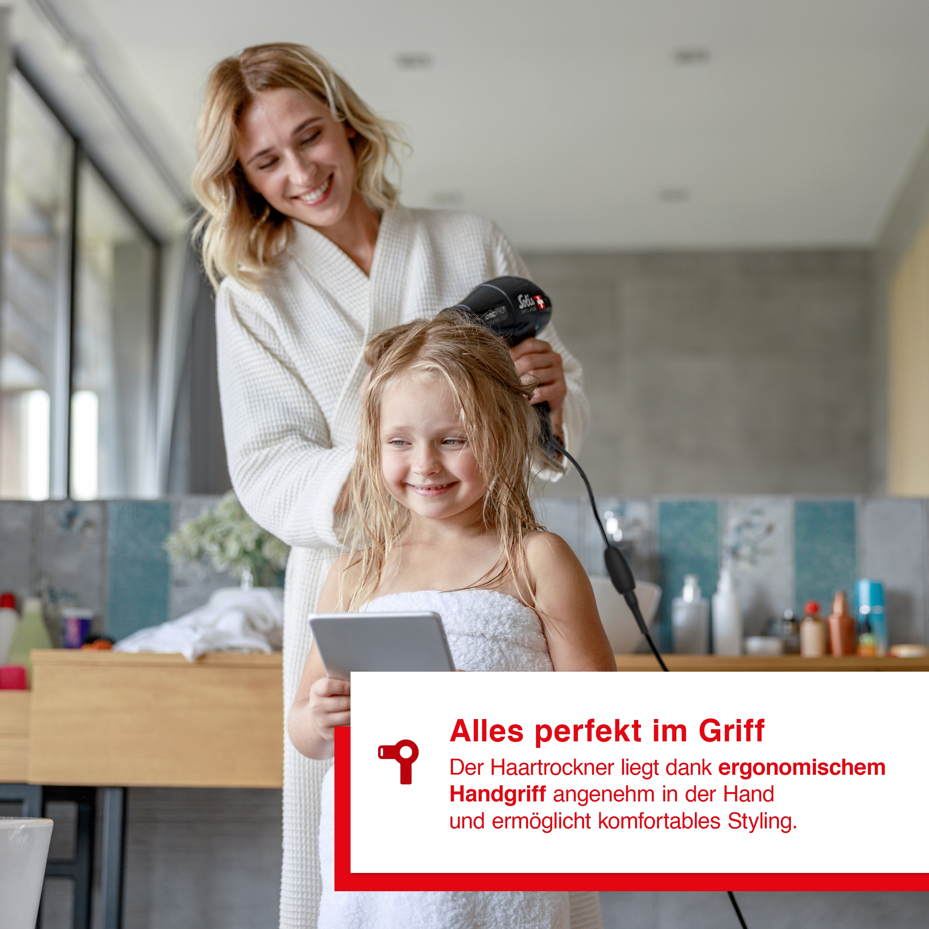 Frau trocknet Mädchen die Haare mit Fön. Badezimmer. Text zum Griff.