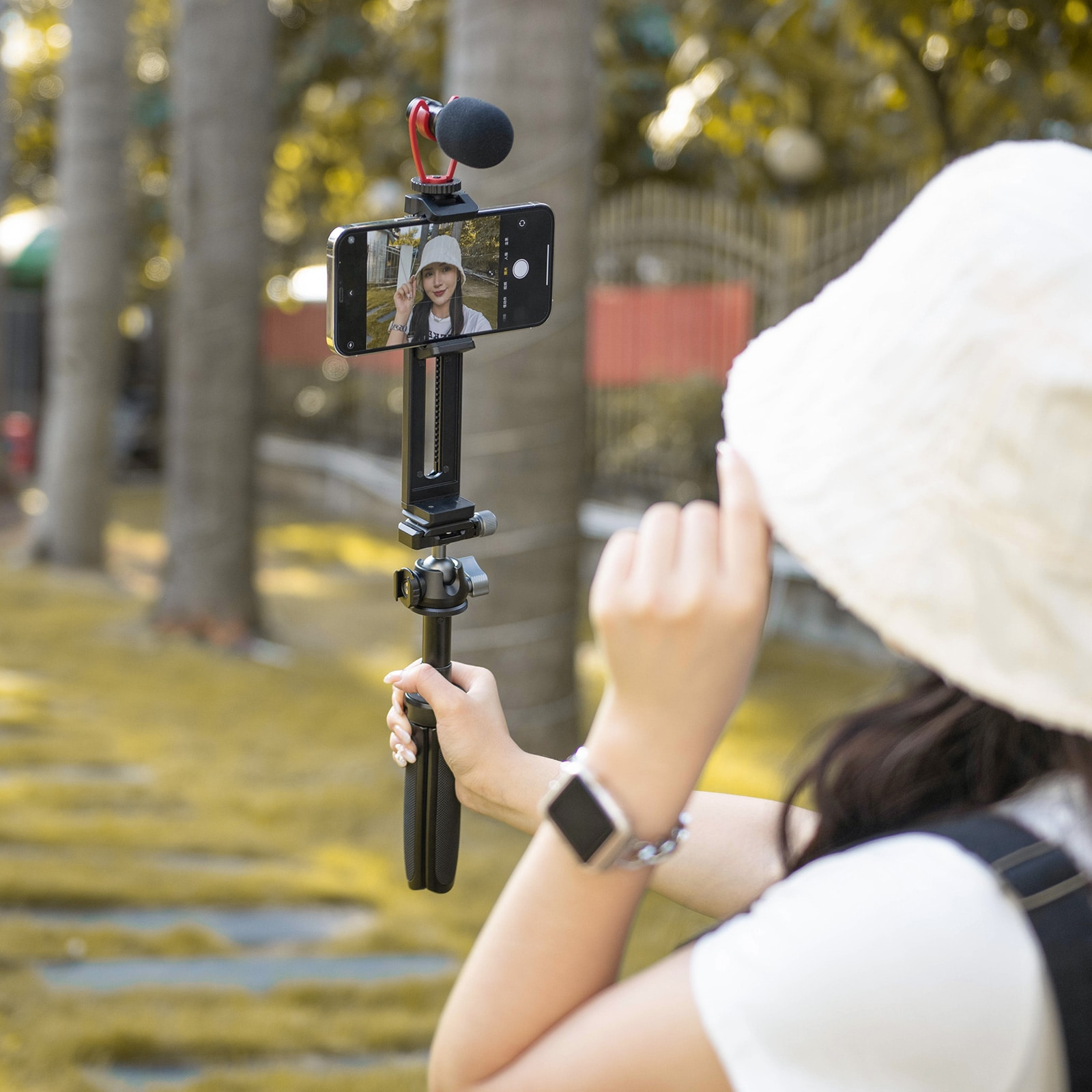 Person holding a phone with a microphone attached to a tripod. The phone shows a video.