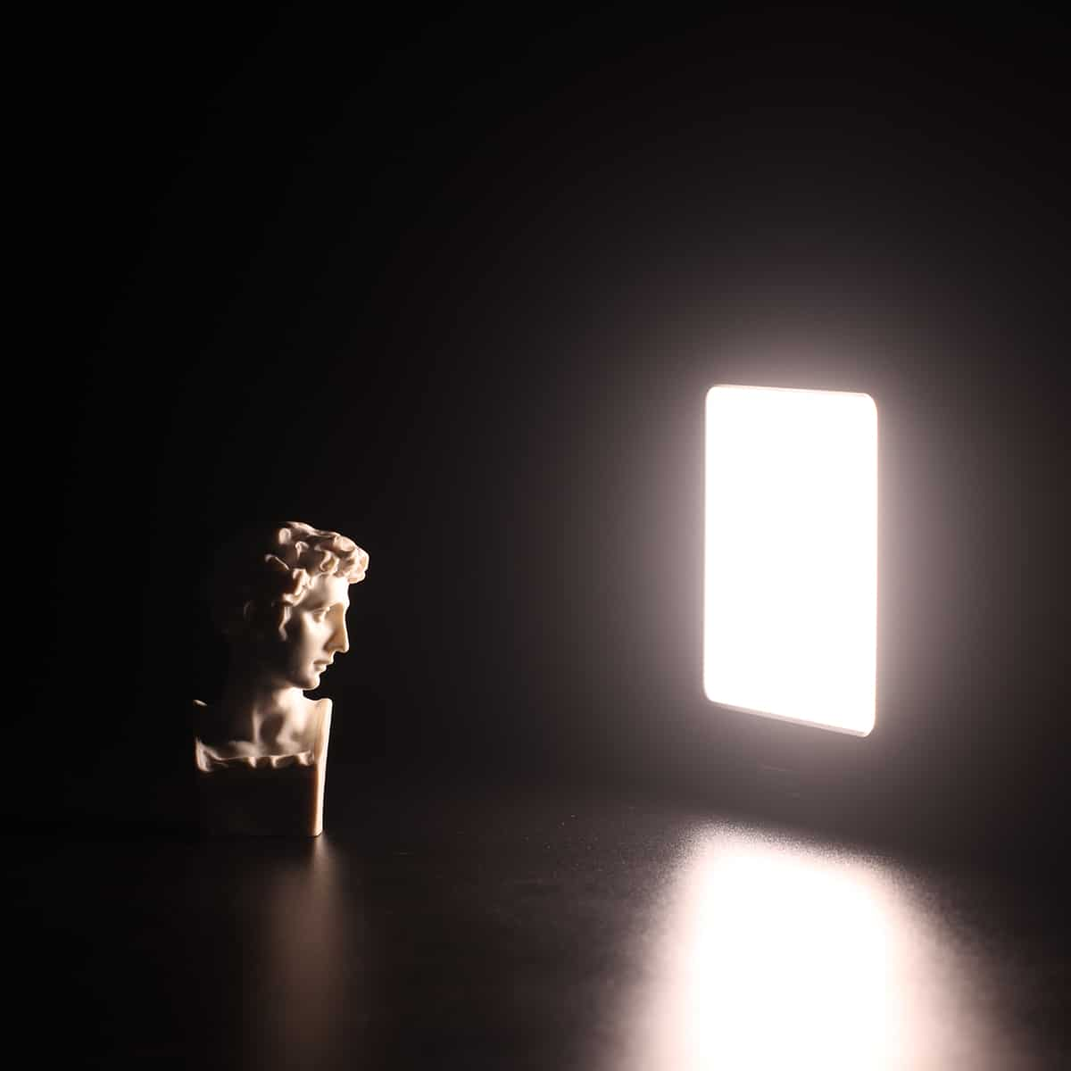 Popiersie mężczyzny ze światłem. Światło jest kwadratowe i jasne. Tło jest czarne.