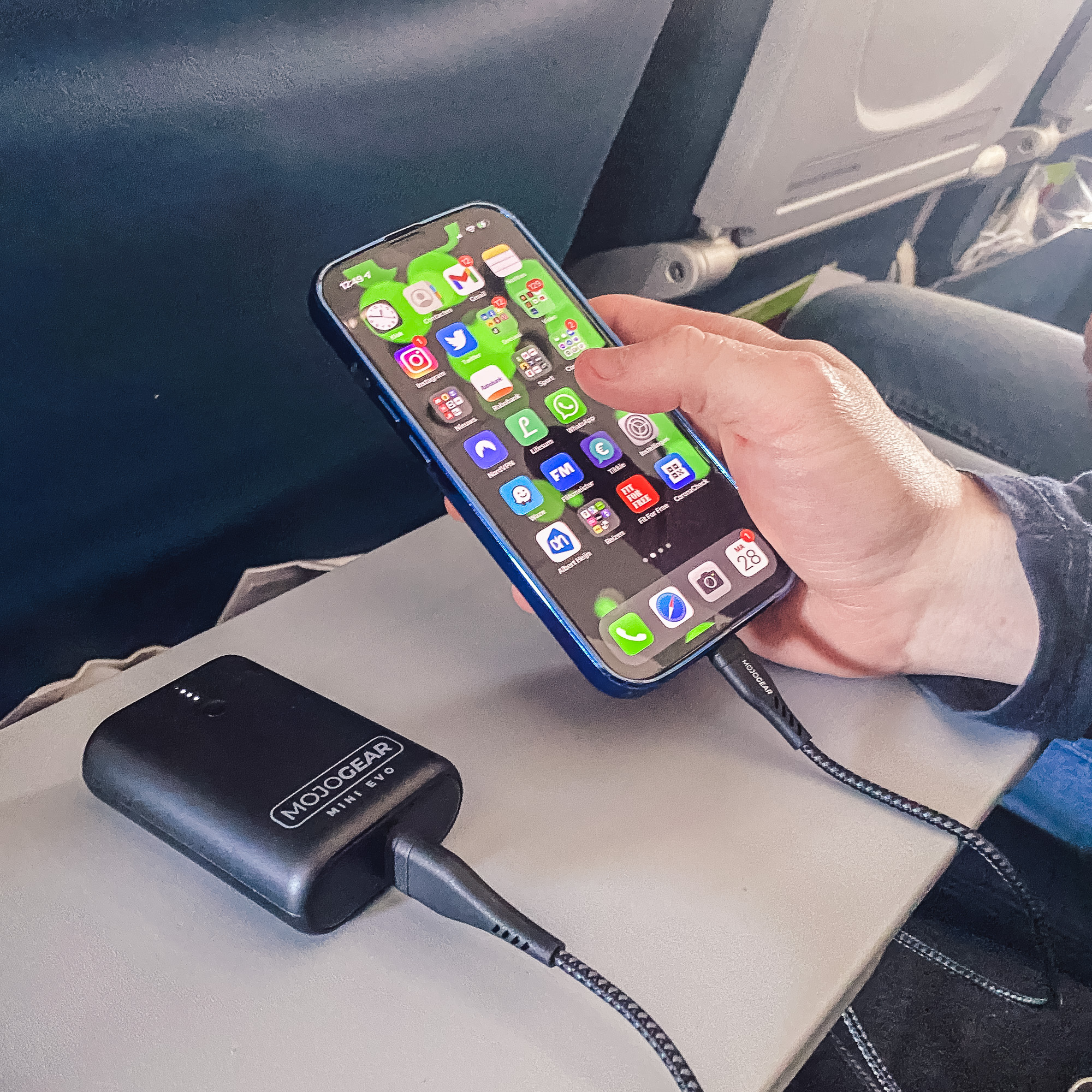 A person holding a blue iPhone charging with a black MotoGear Mini Evo power bank.