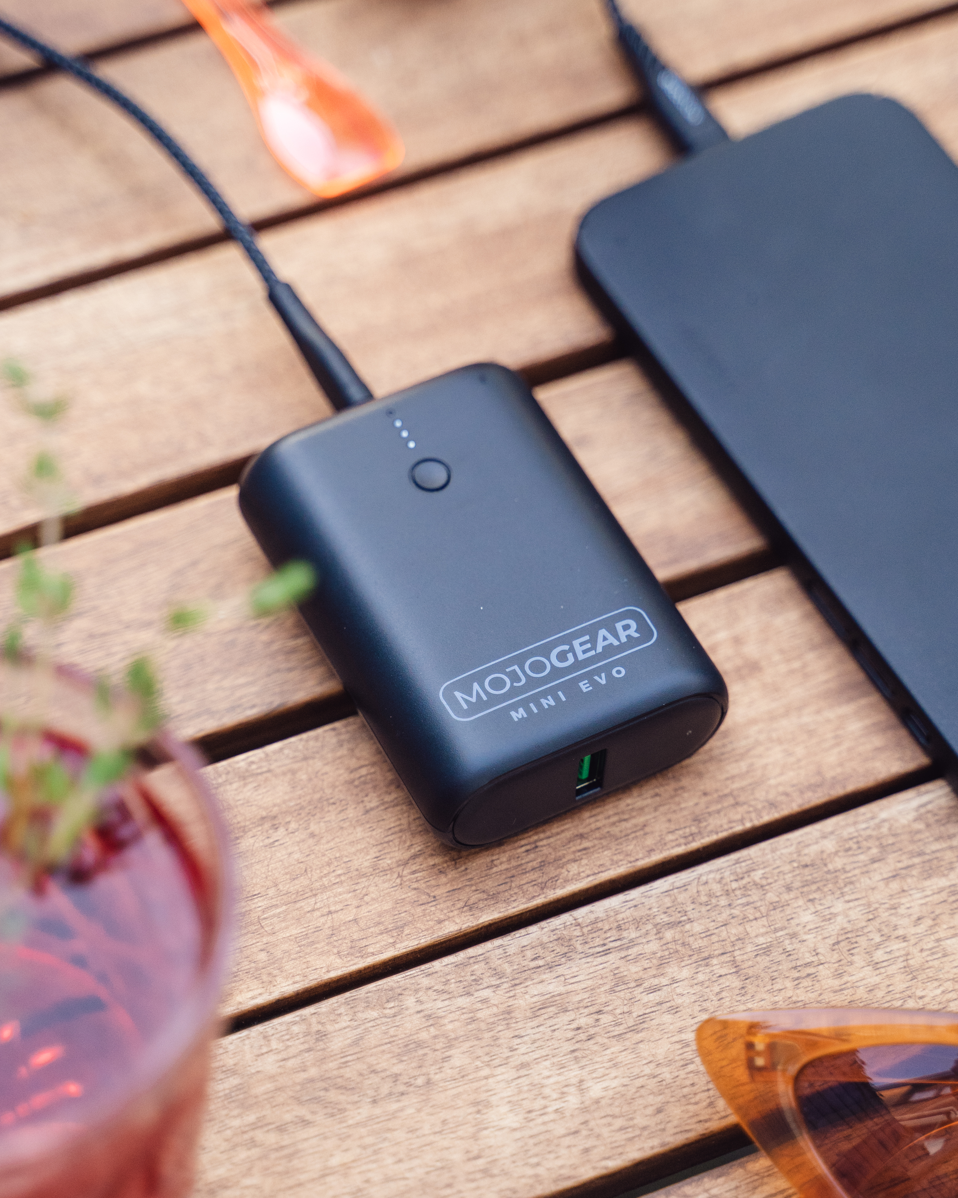 Black MojoGear Mini Evo power bank charging a black phone. Wooden background.