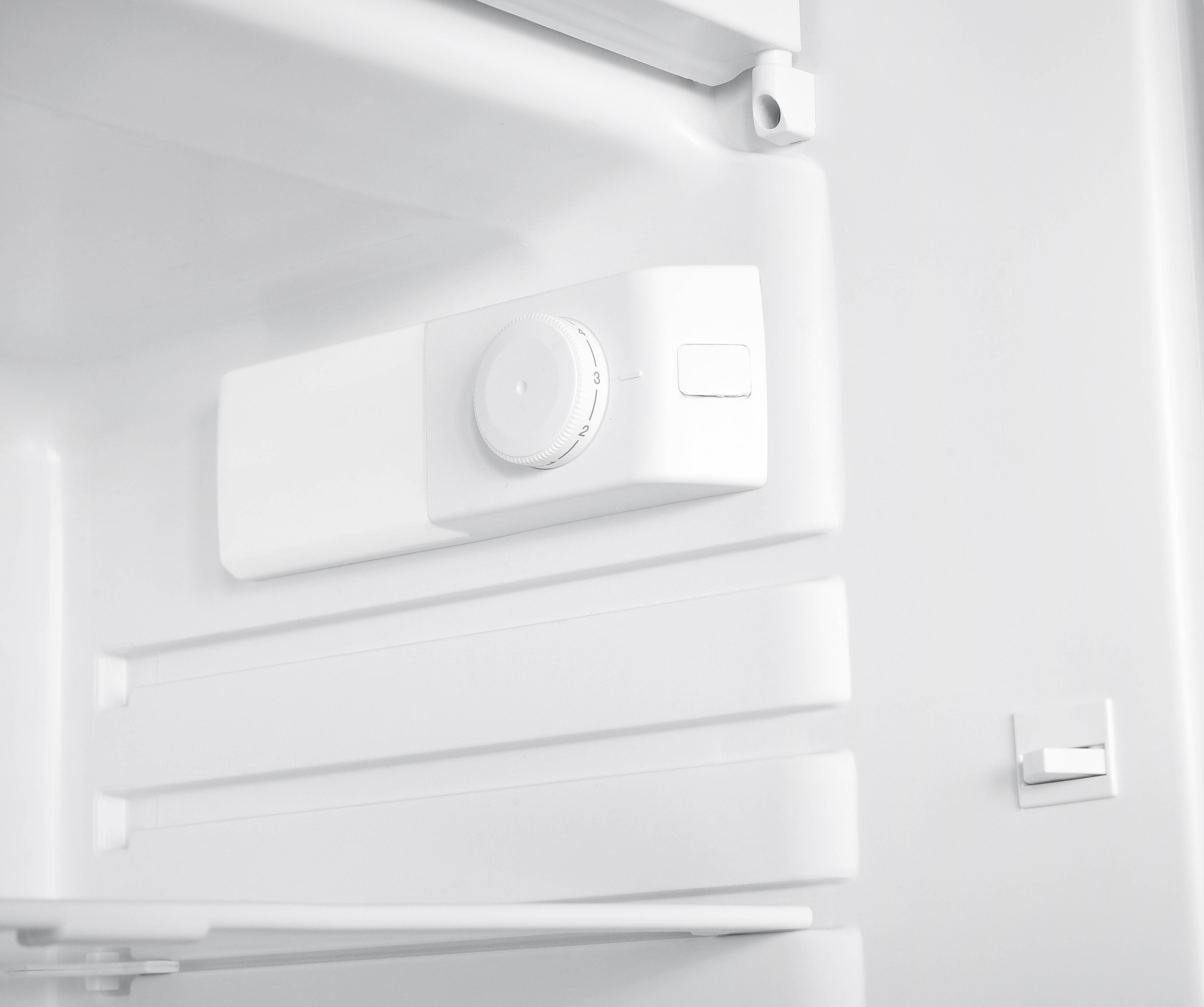 An open, white refrigerator interior. A control panel with a dial is visible on the wall.