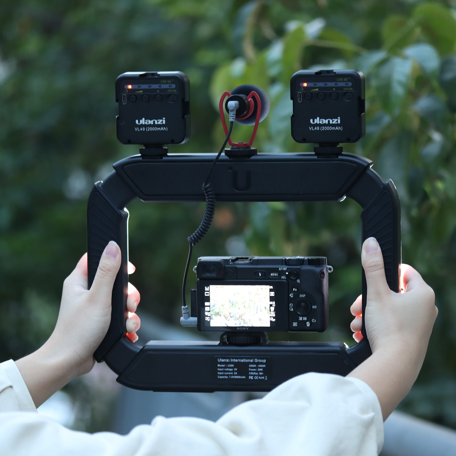 Una persona tiene un rig per fotocamera nero con luci e microfono.