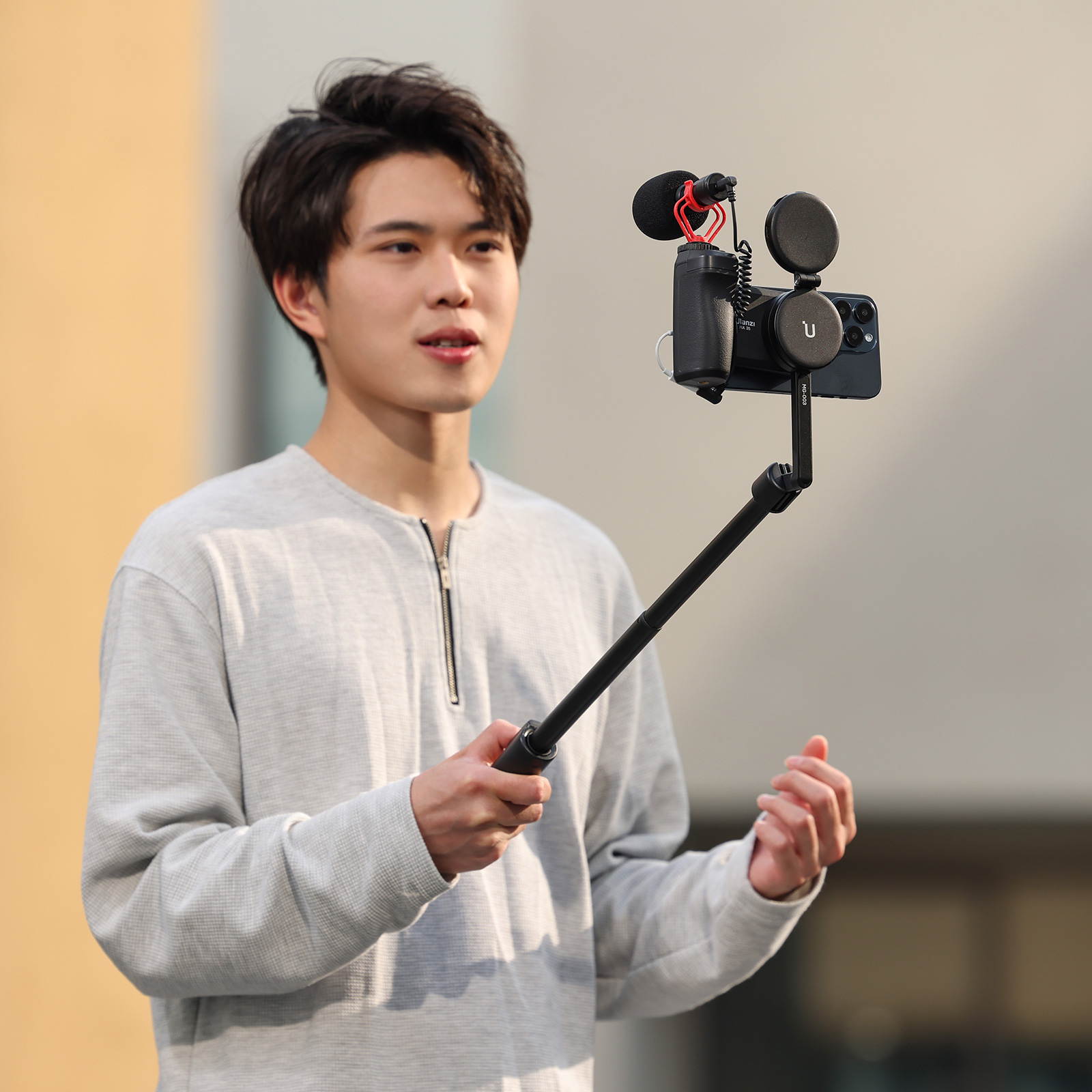 Mężczyzna trzymający aparat z mikrofonem, na patyku do selfie, w plenerze.