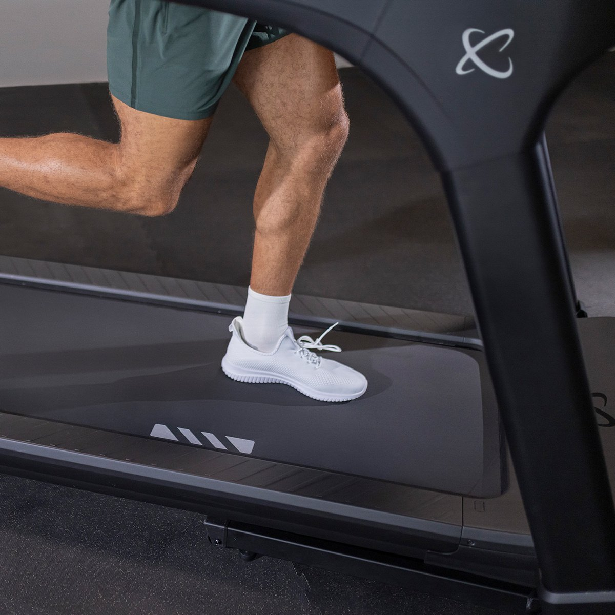 A person running on a treadmill with white shoes. The treadmill is black and grey.