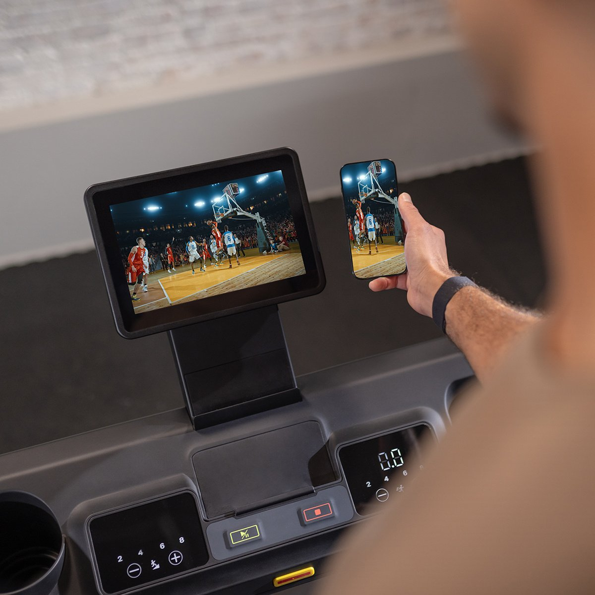 Man on treadmill watching basketball on a tablet, and a phone displaying same image.