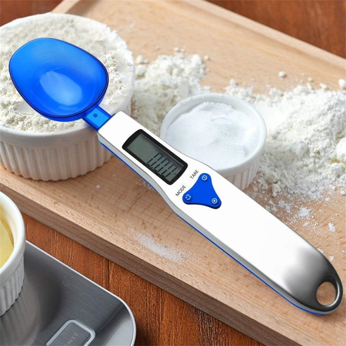 Eine digitale Löffelwaage mit blauem Löffel, weißem Körper und Zutaten wie Mehl.