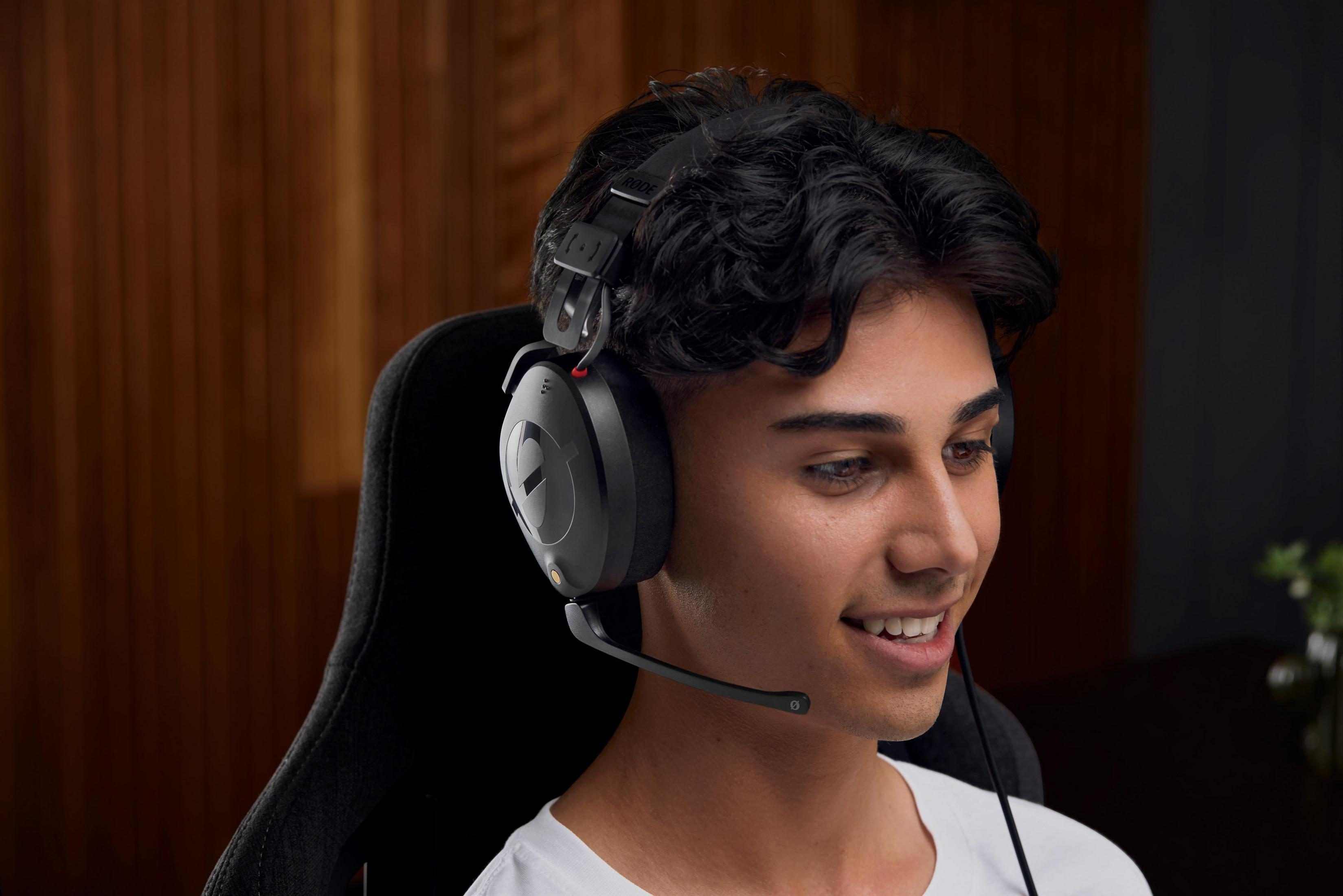 Młody mężczyzna w czarnych słuchawkach do gier z mikrofonem. Uśmiecha się.