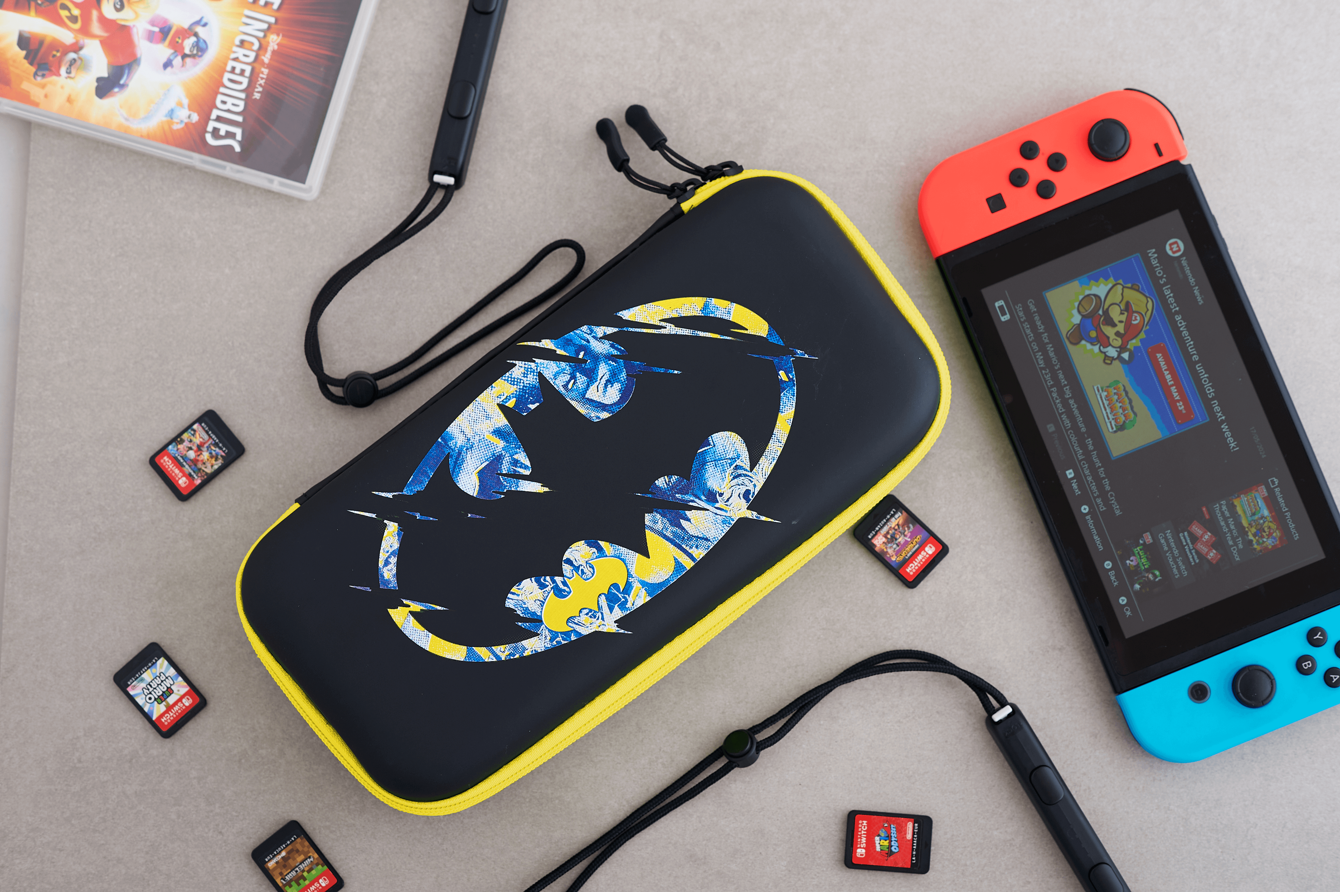 Un estuche negro con el logo de Batman, una Switch y cartuchos de juego en una superficie.