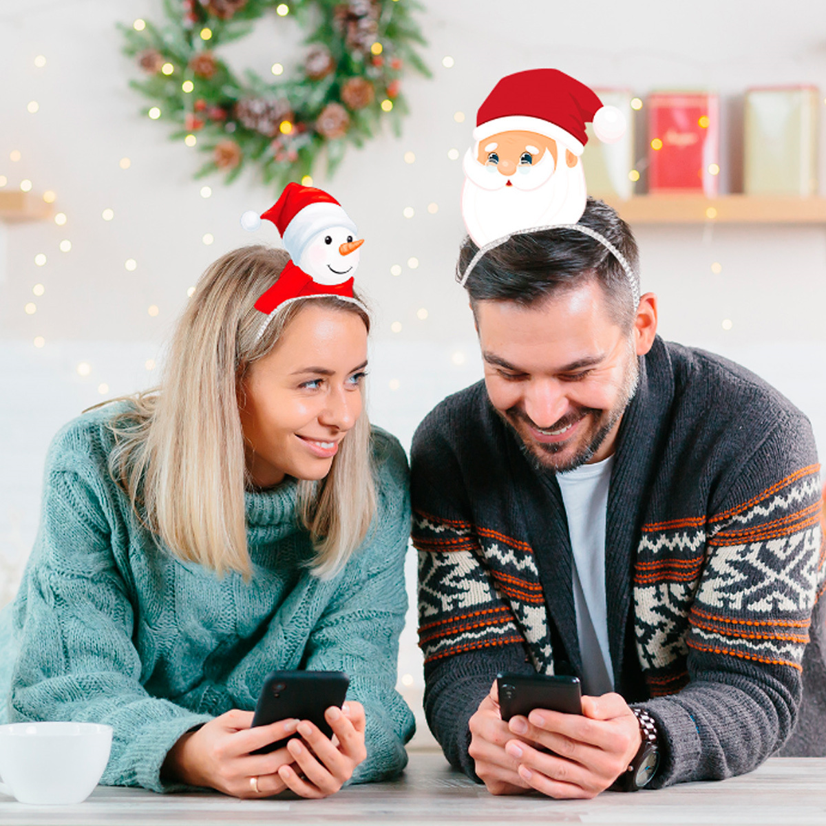Ein Paar mit Weihnachts-Haarbändern. Sie schauen auf ihre Handys.
