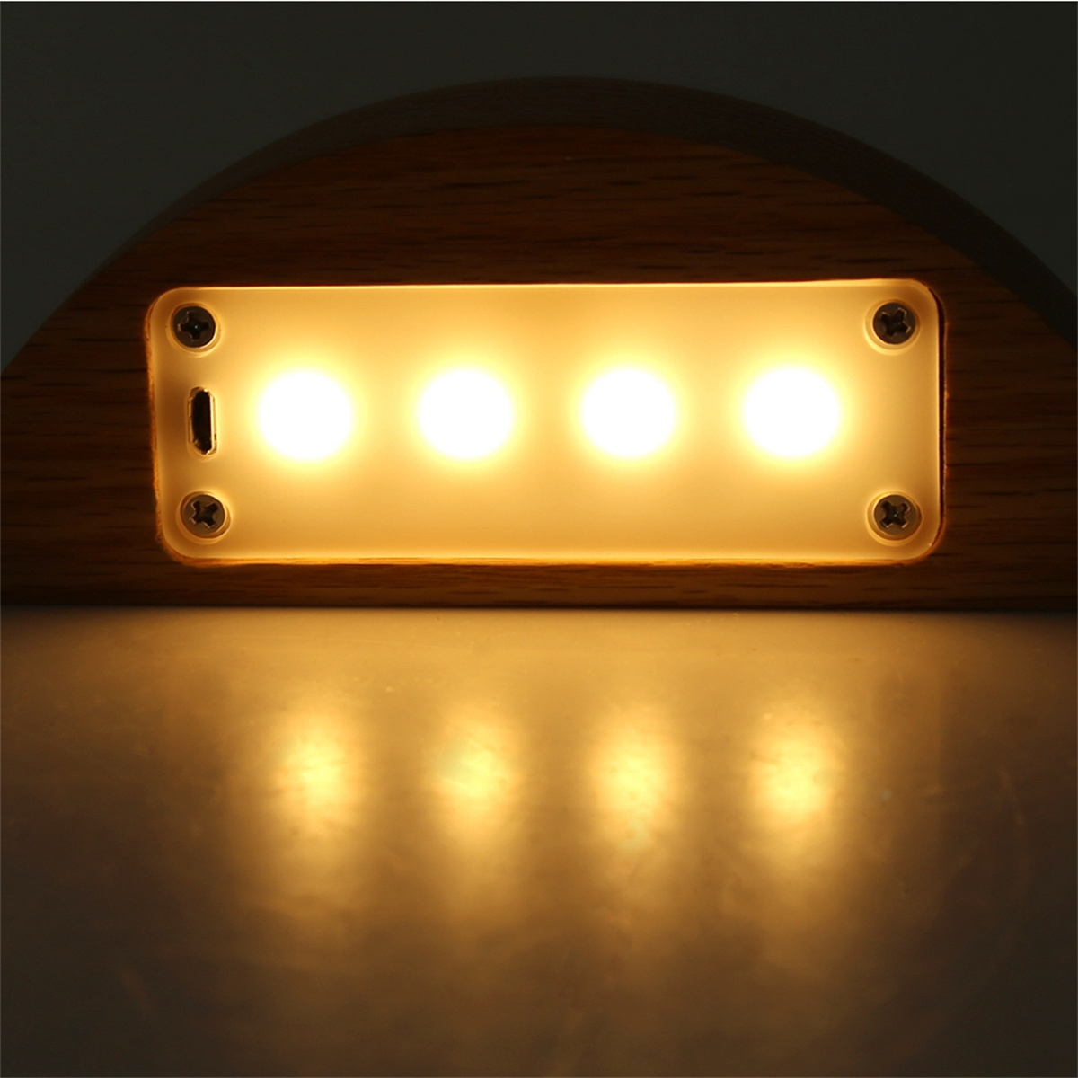 Ein Einbaustrahler mit vier hellen Lichtern. Es ist in eine Holzoberfläche eingebettet.