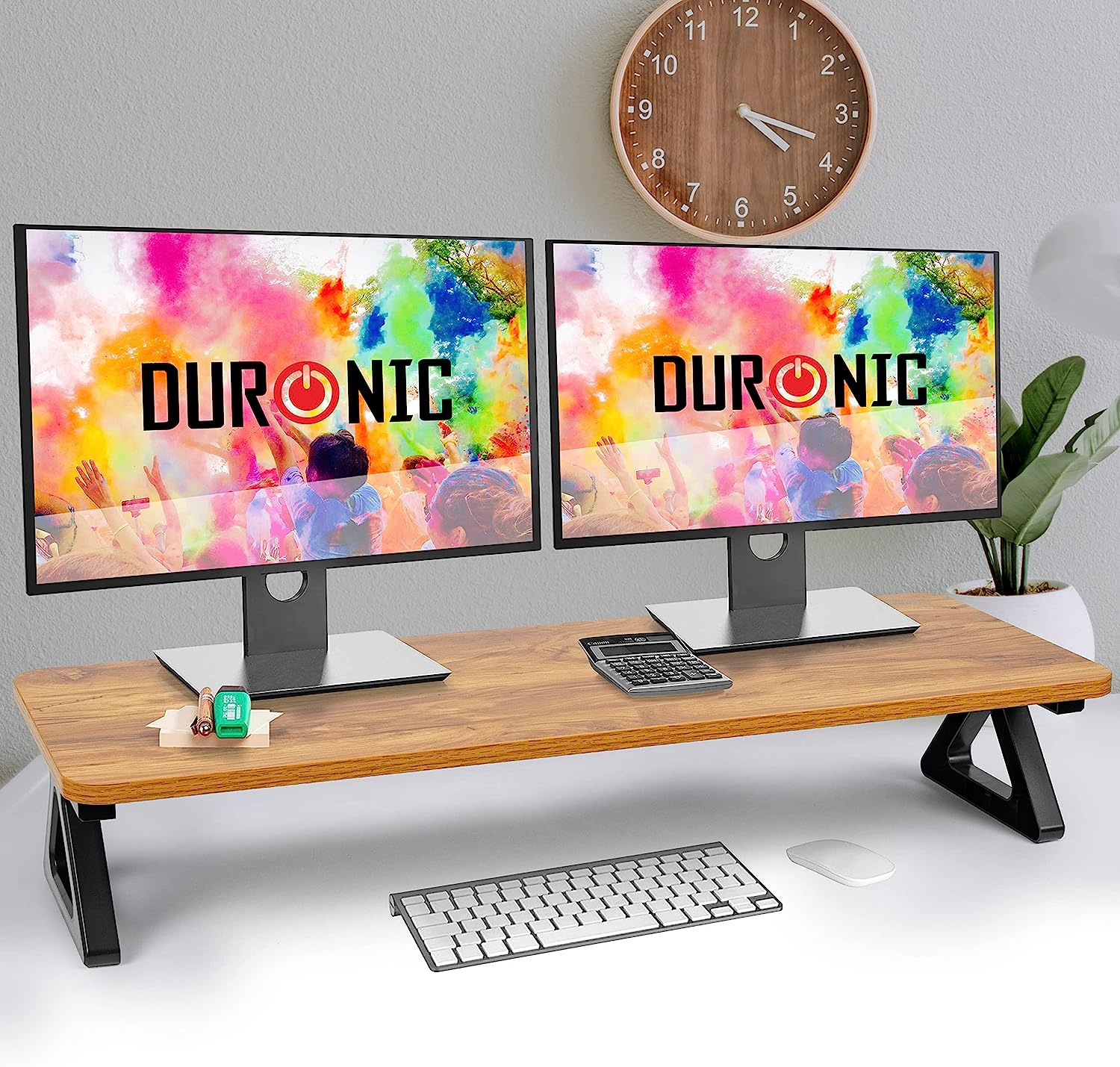 Zwei Monitore stehen auf einem Holzschreibtisch mit Tastatur, Maus und Uhr im Hintergrund.